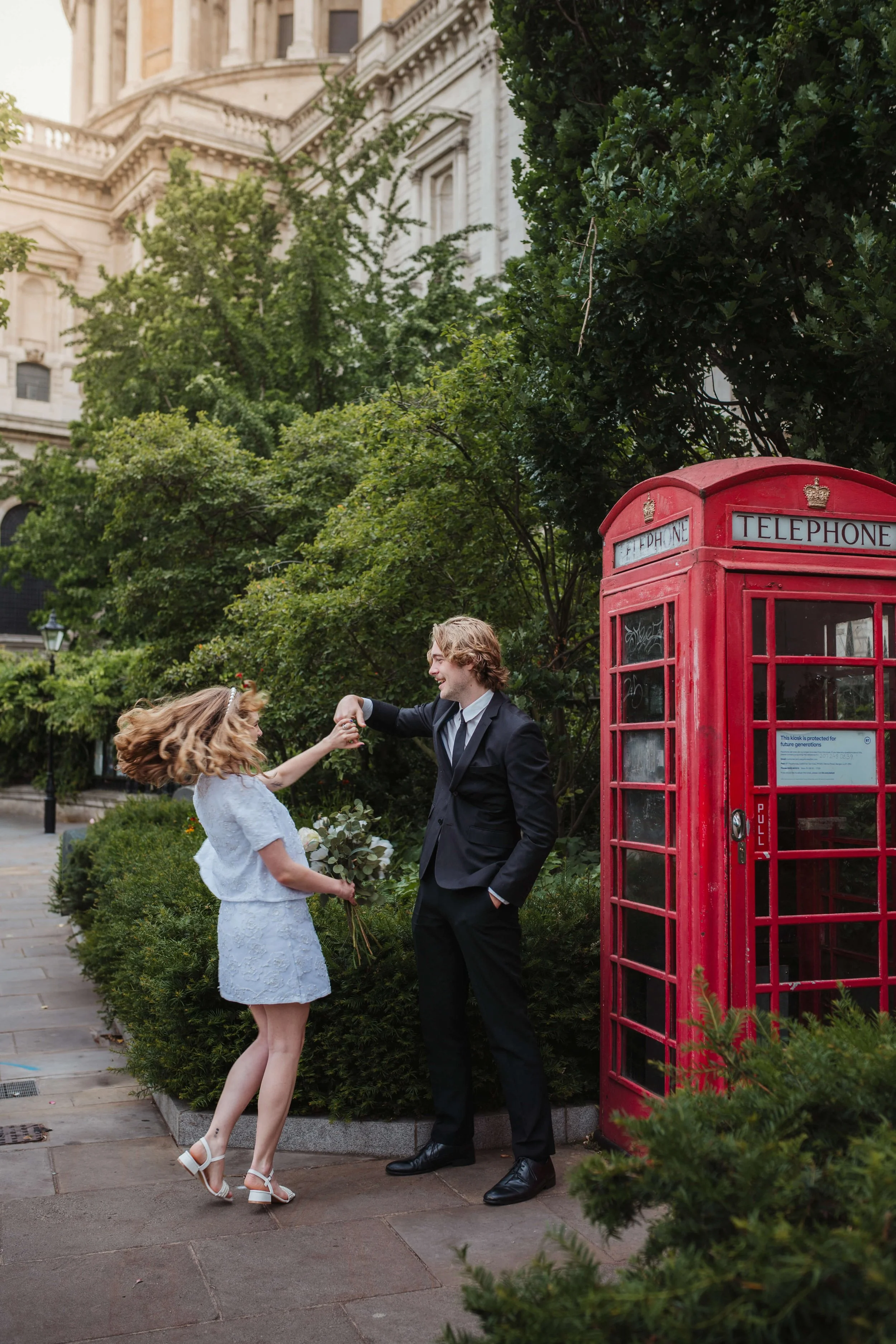groom twirls Bride next to Red British telephone box in London outside St Pauls Cathedral 