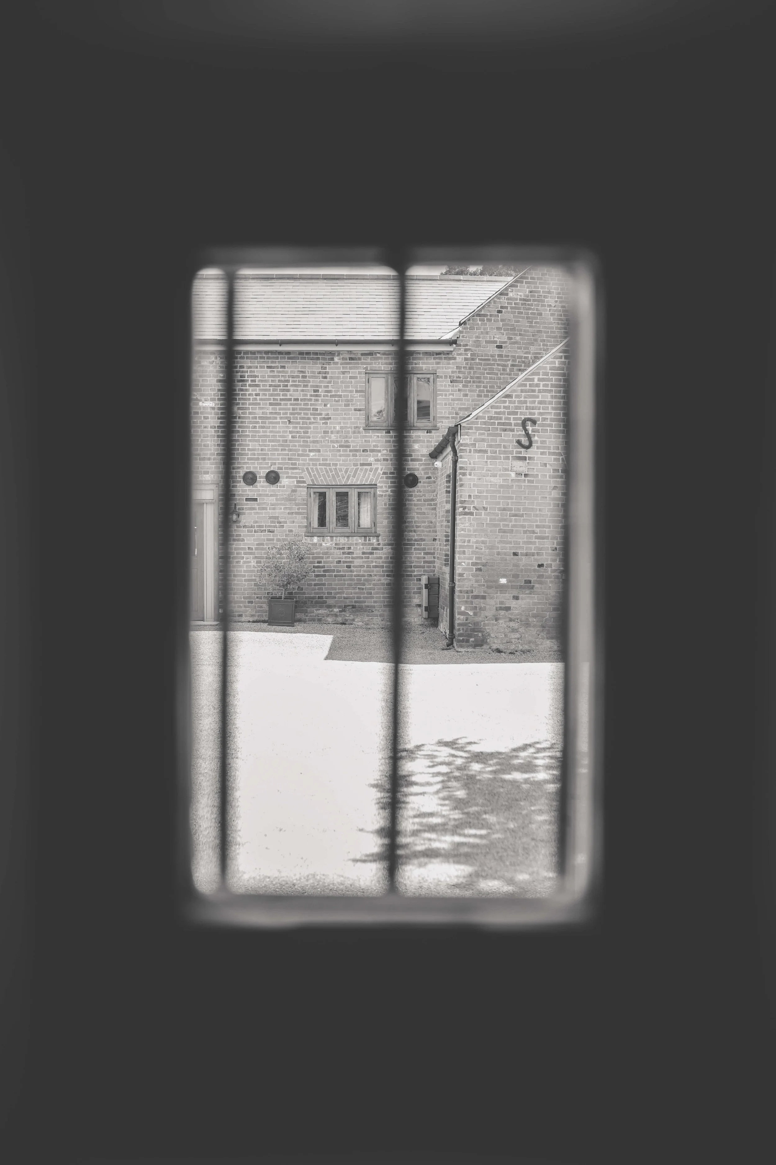 View of a brick house through a window with bars, in black and white.