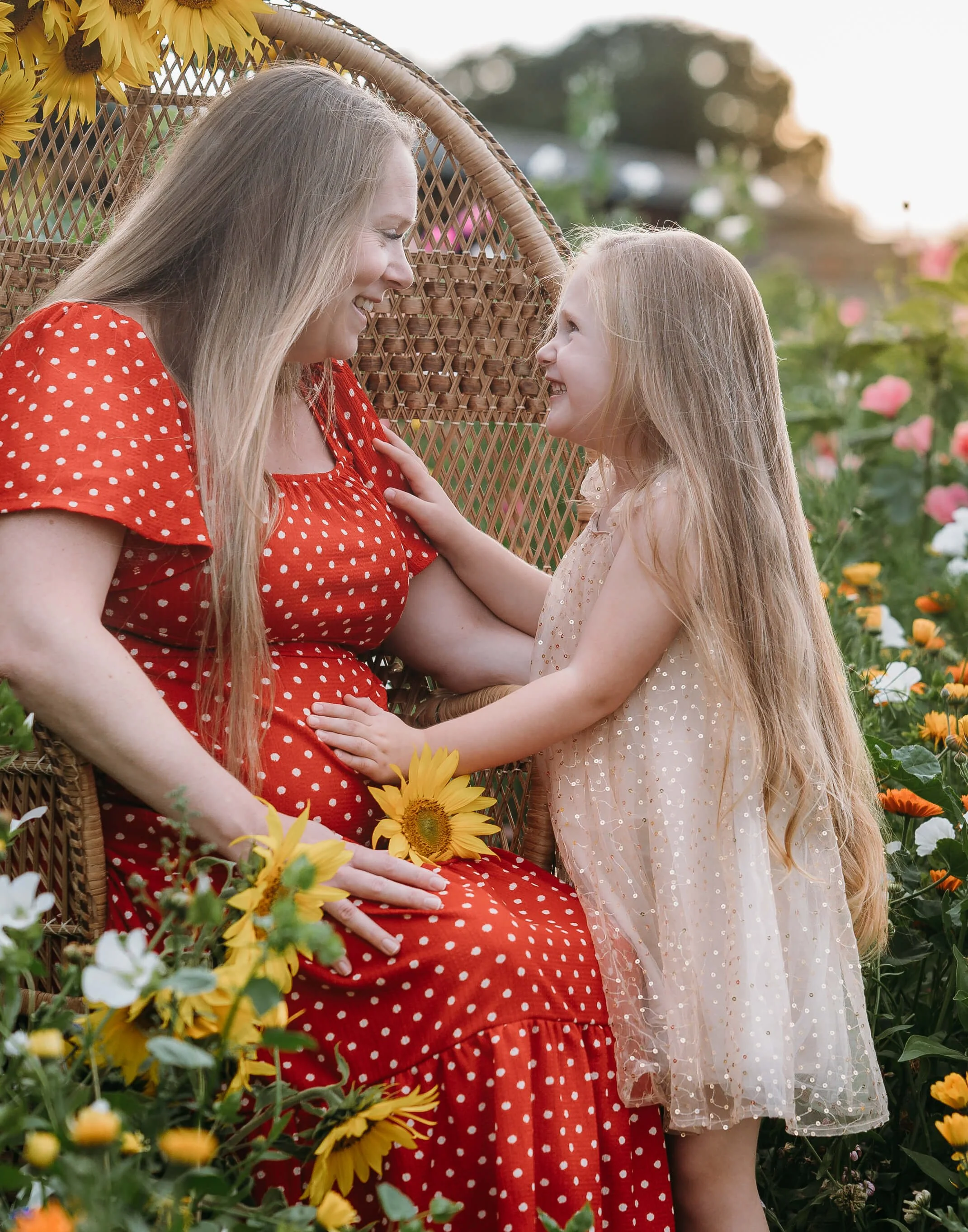 child lays hand on mums pregnant belly in sunflower field 