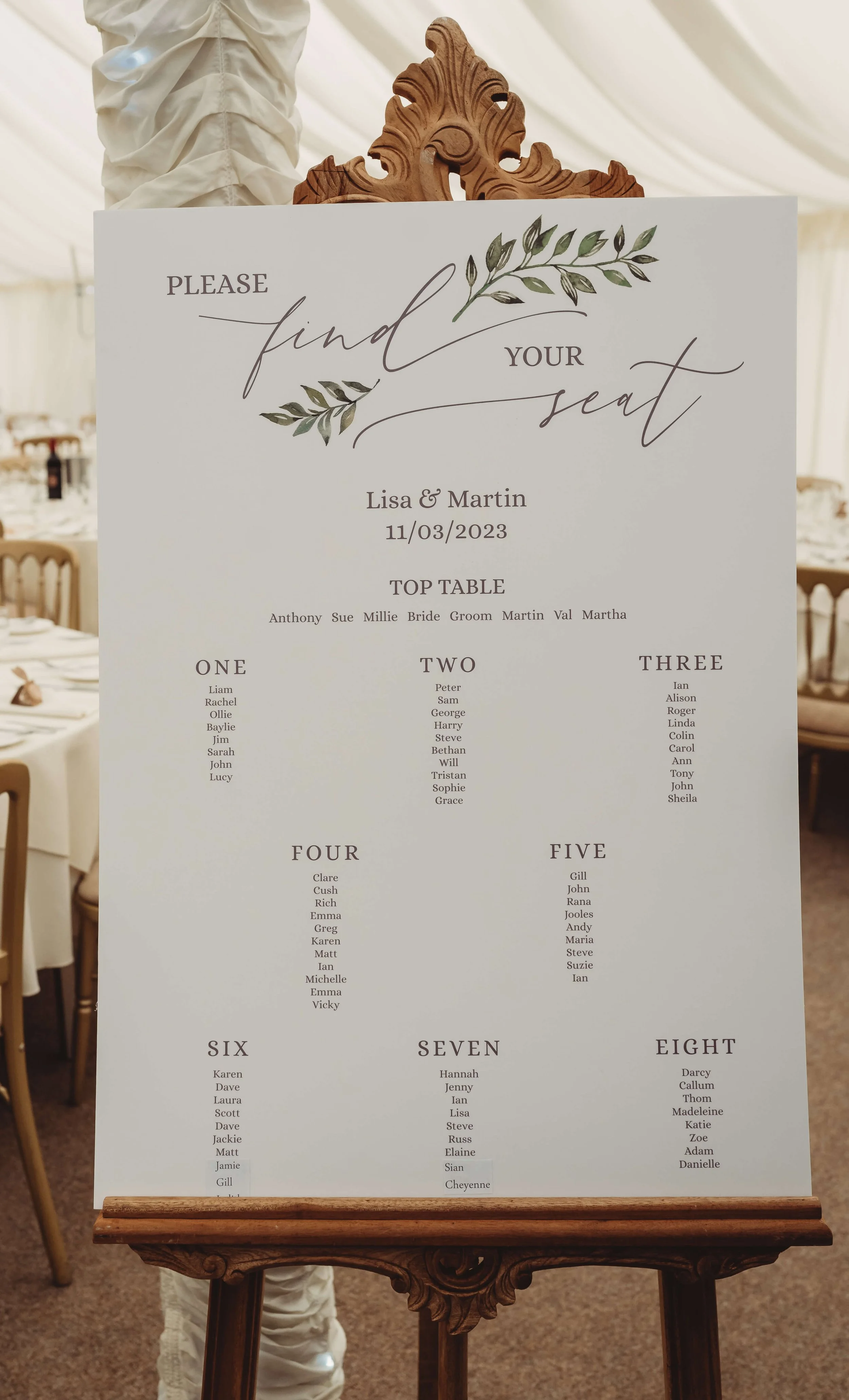 Wedding seating chart with the title 'Please find your seat' decorated with green leaves, listing names under tables numbered one through eight.