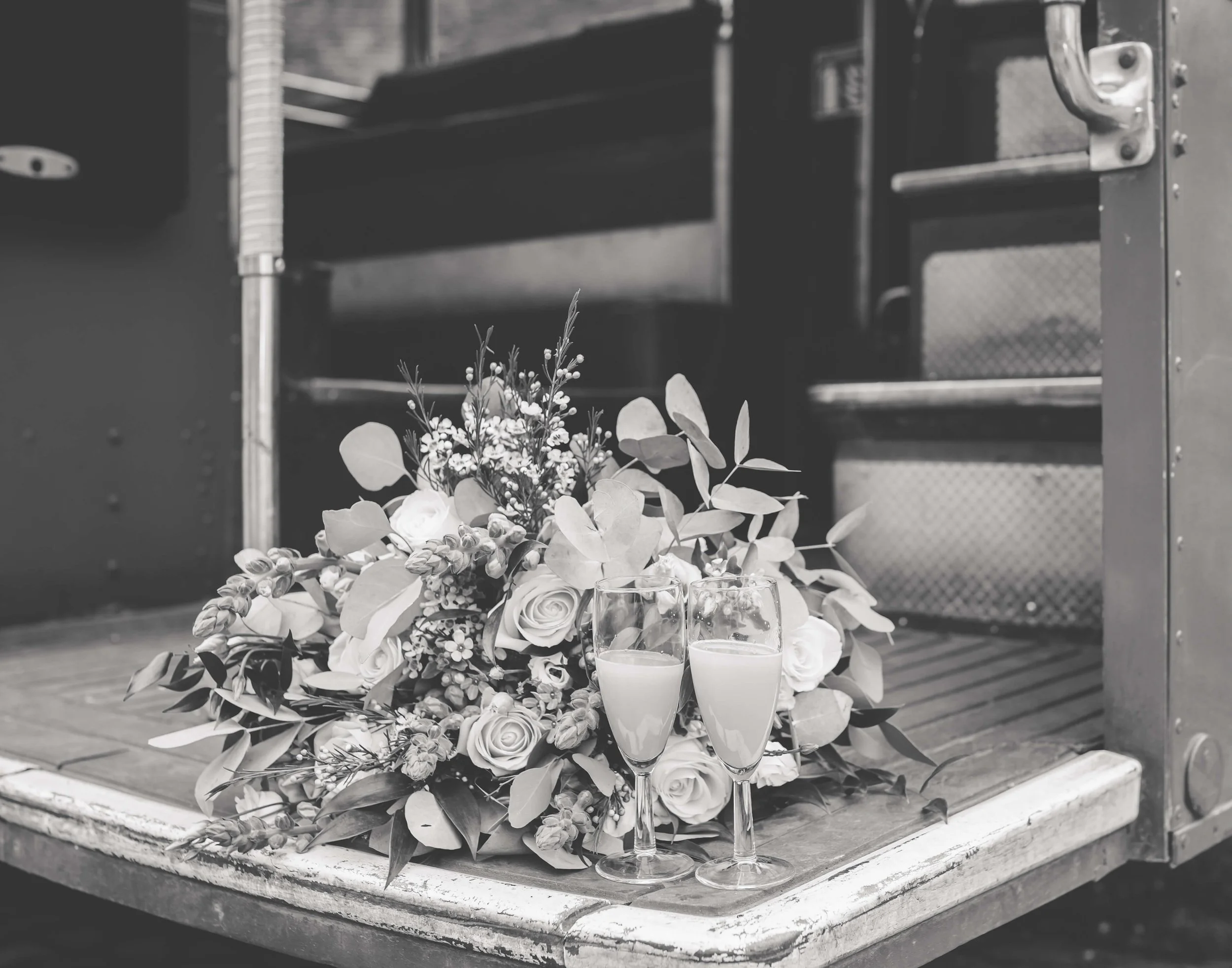 A bouquet of flowers and two glasses of champagne on a truck's tailgate.