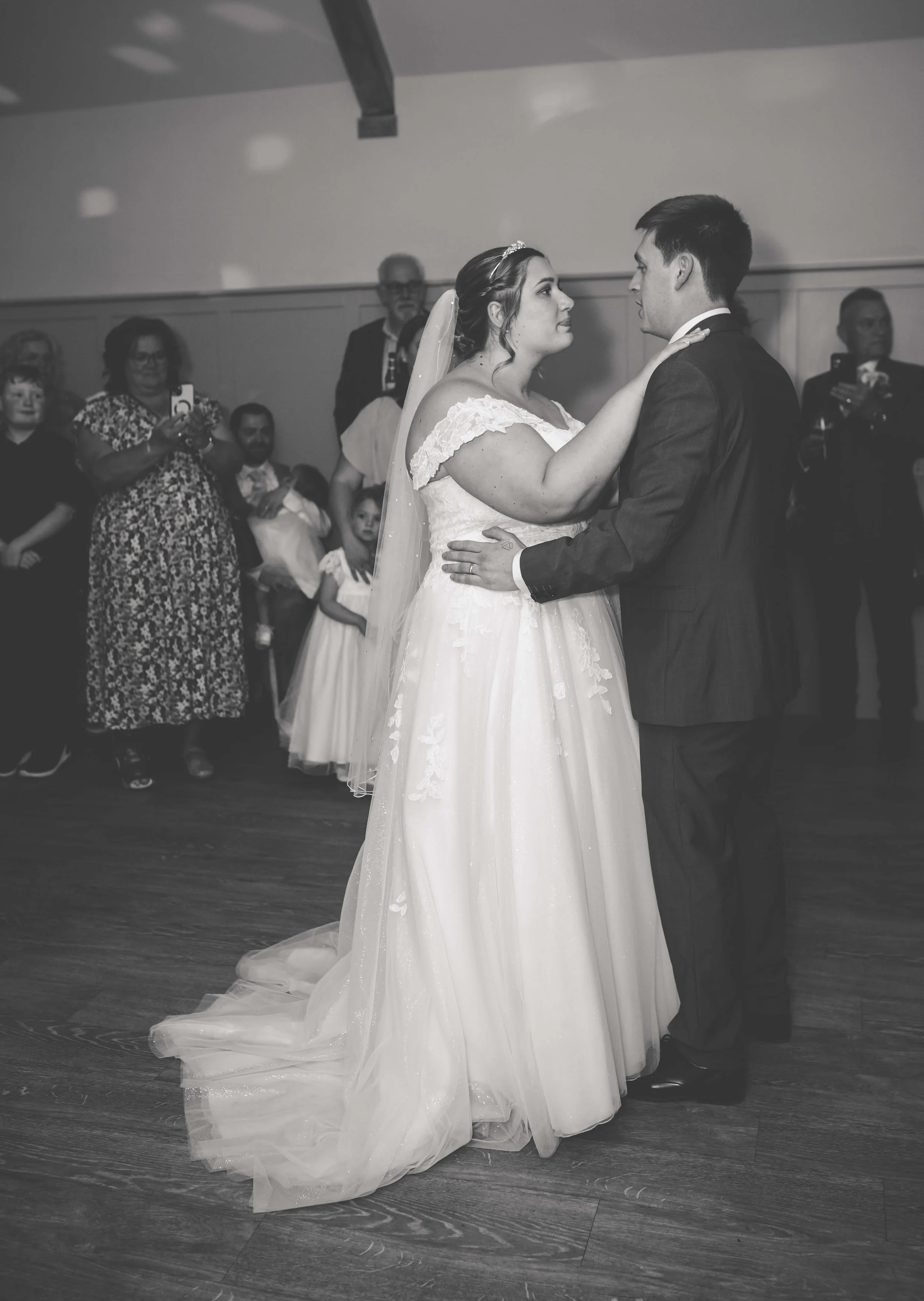 A bride and groom sharing their first dance at their wedding reception, surrounded by family and friends.