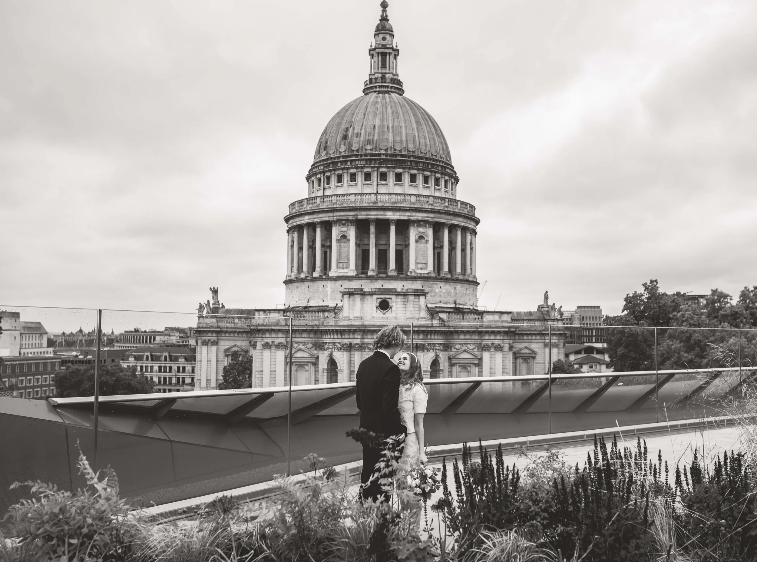 A couple dancing on a rooftop with St. Paul's Cathedral in London in the background, in black and white.