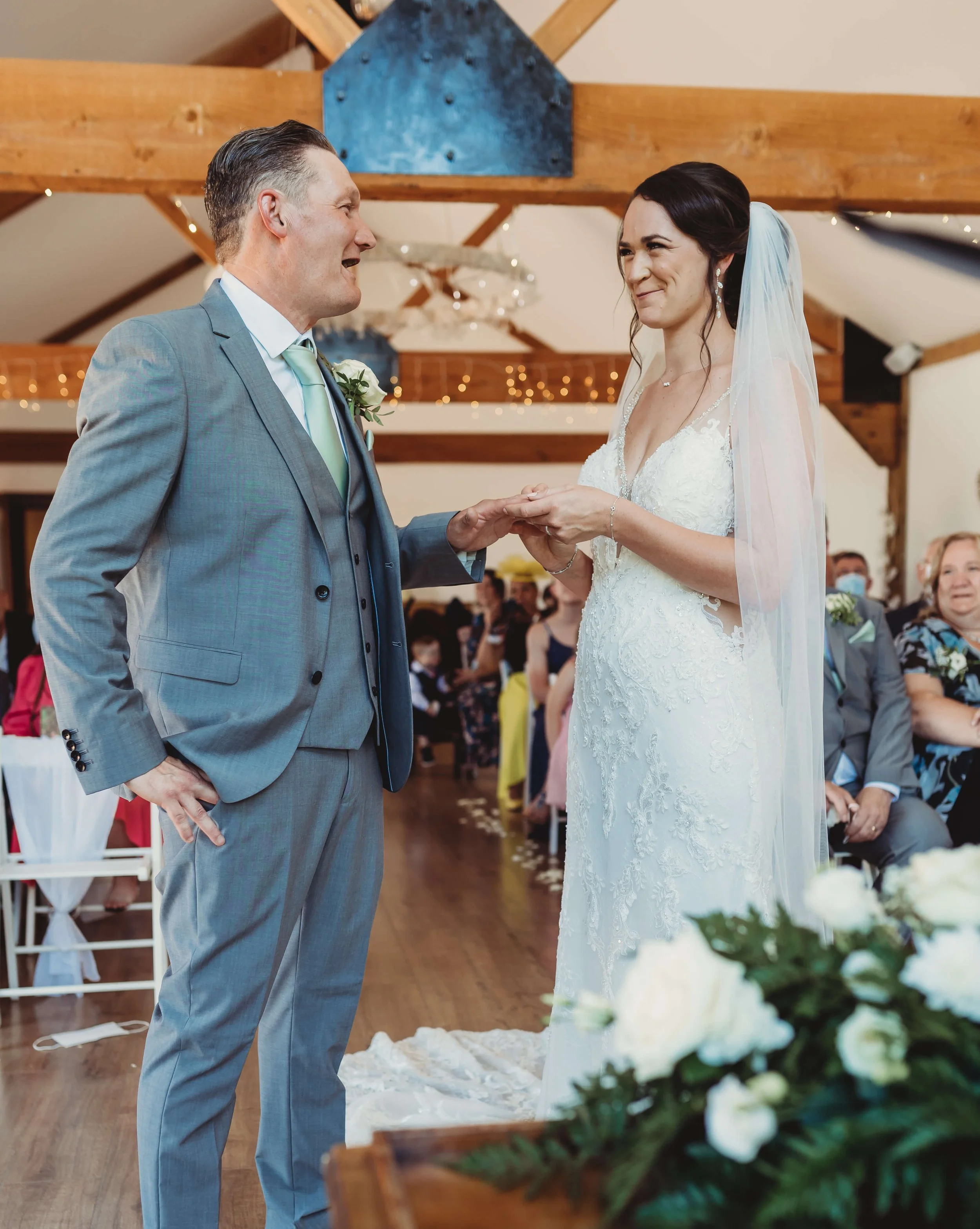 A bride and groom exchanging vows during their wedding ceremony inside a rustic venue with wooden beams and string lights.