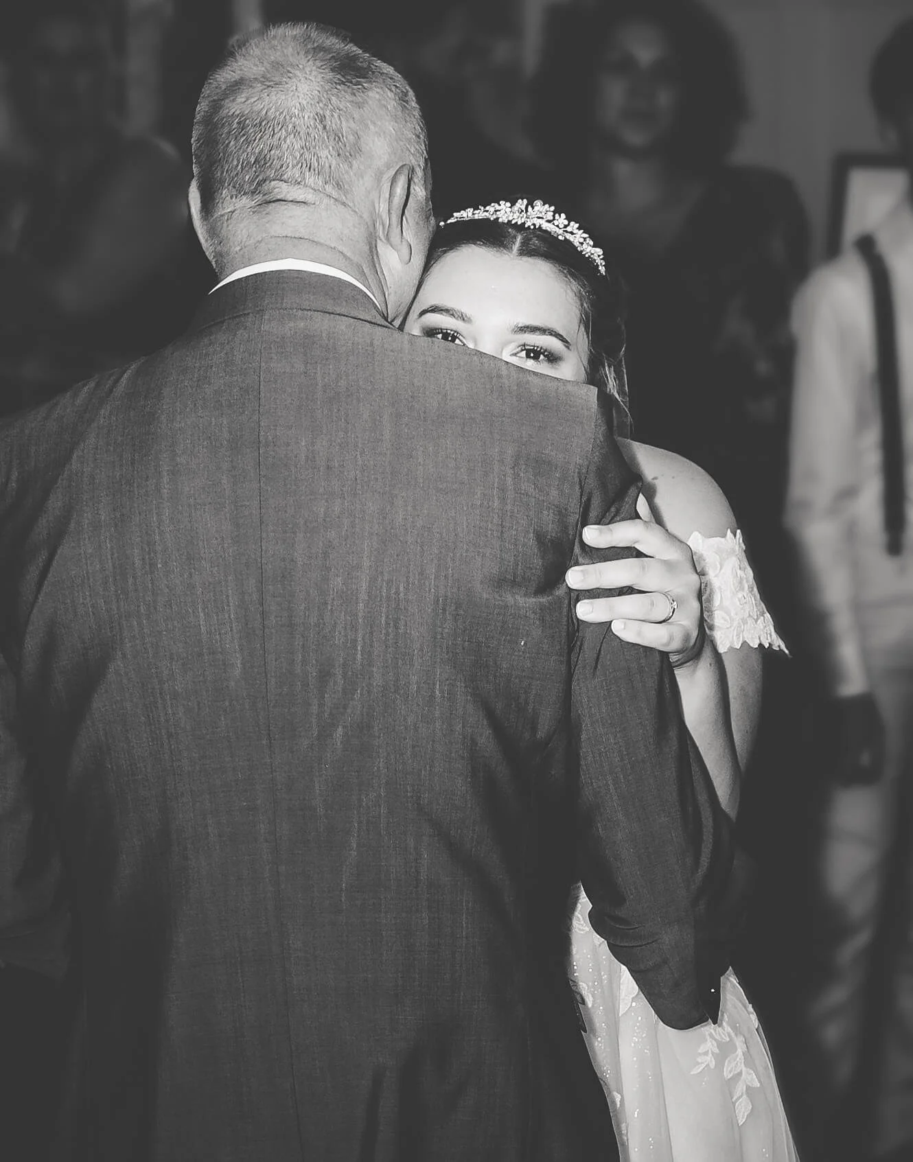 A bride and an older man, possibly her father, dancing together at her wedding, with the bride looking over his shoulder and smiling.