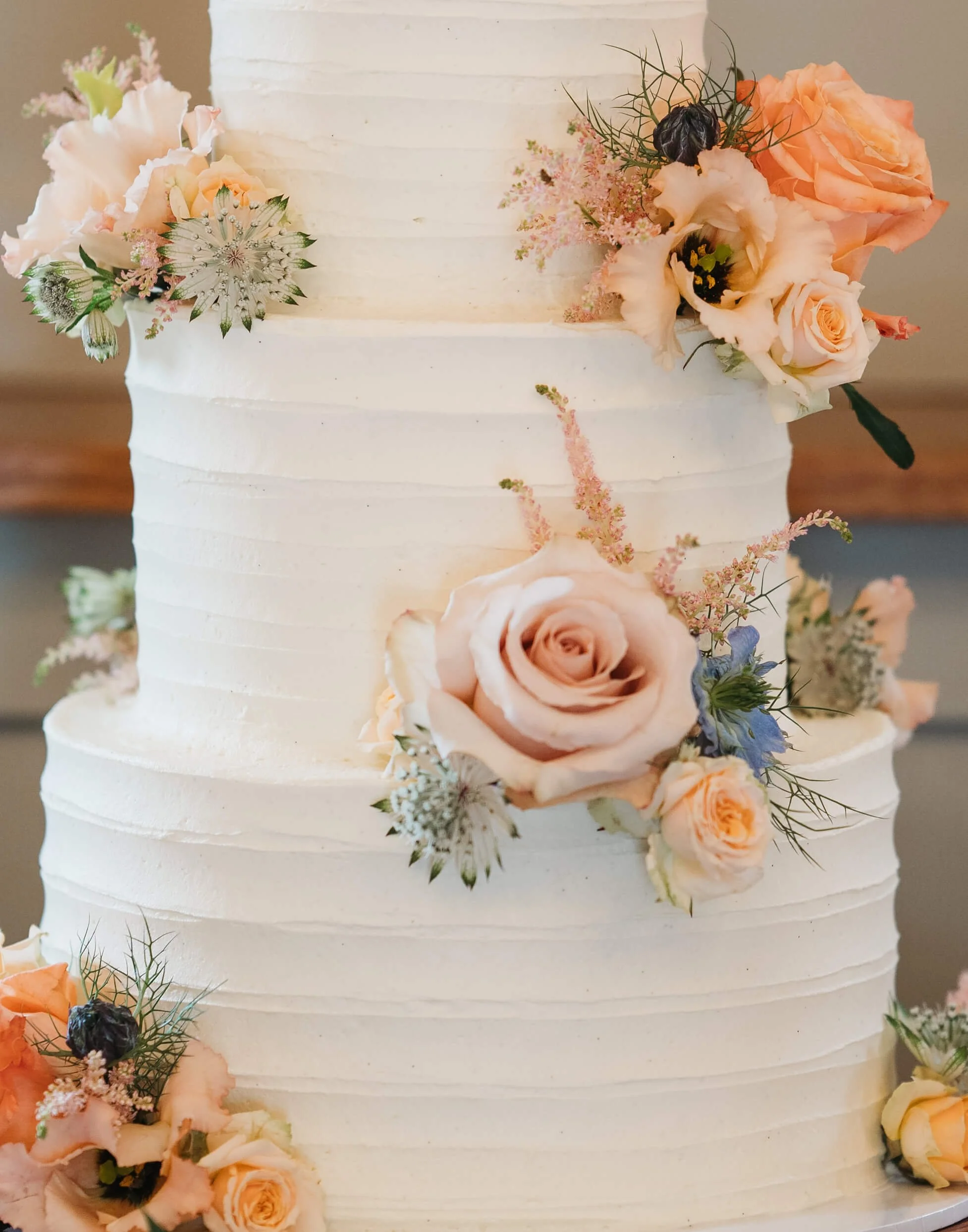 Wedding cake decorated with peach and cream roses, pastel flowers, and greenery.