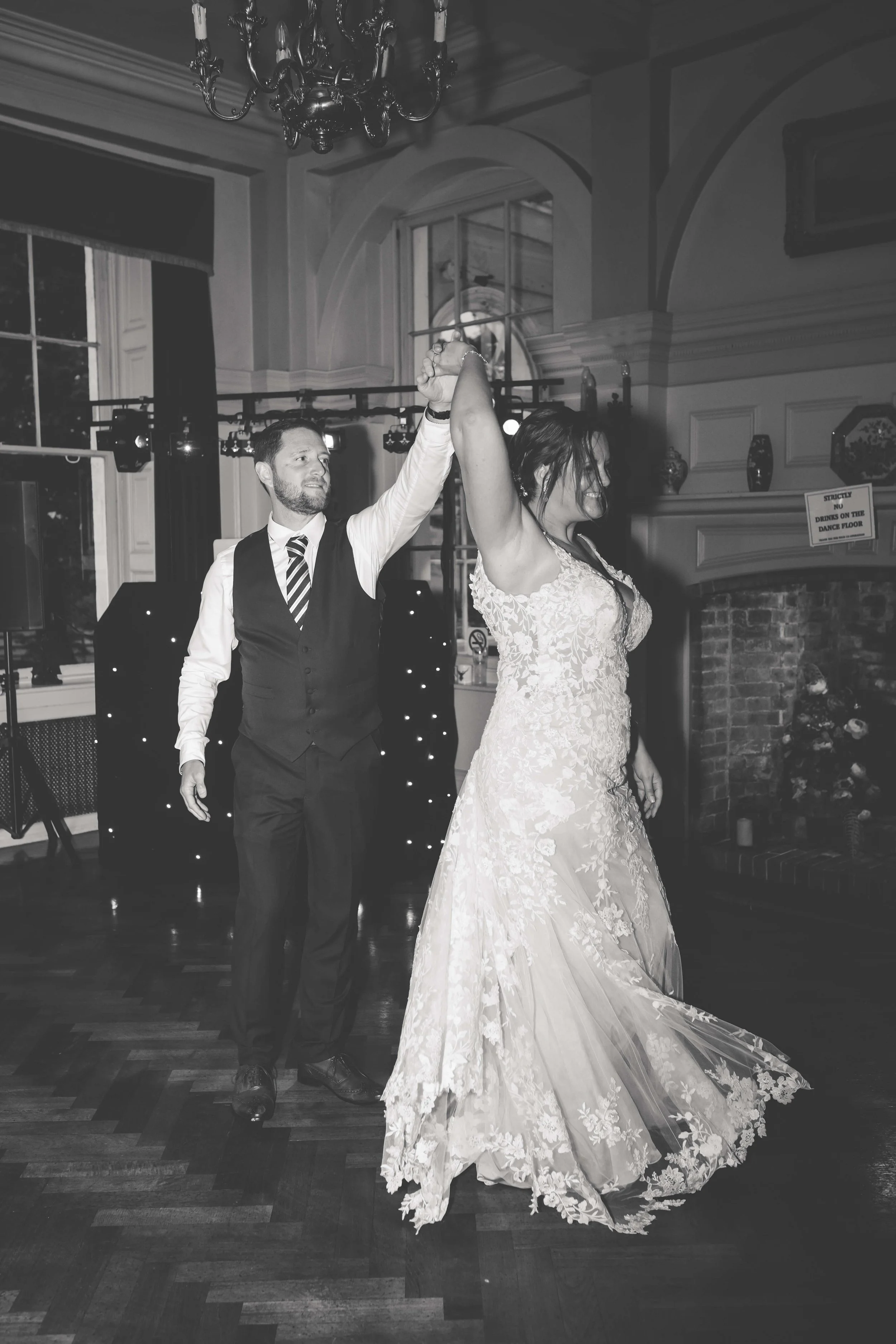 A bride and groom dancing, with the groom holding the bride's hand in the air, in a decorated indoor wedding venue.