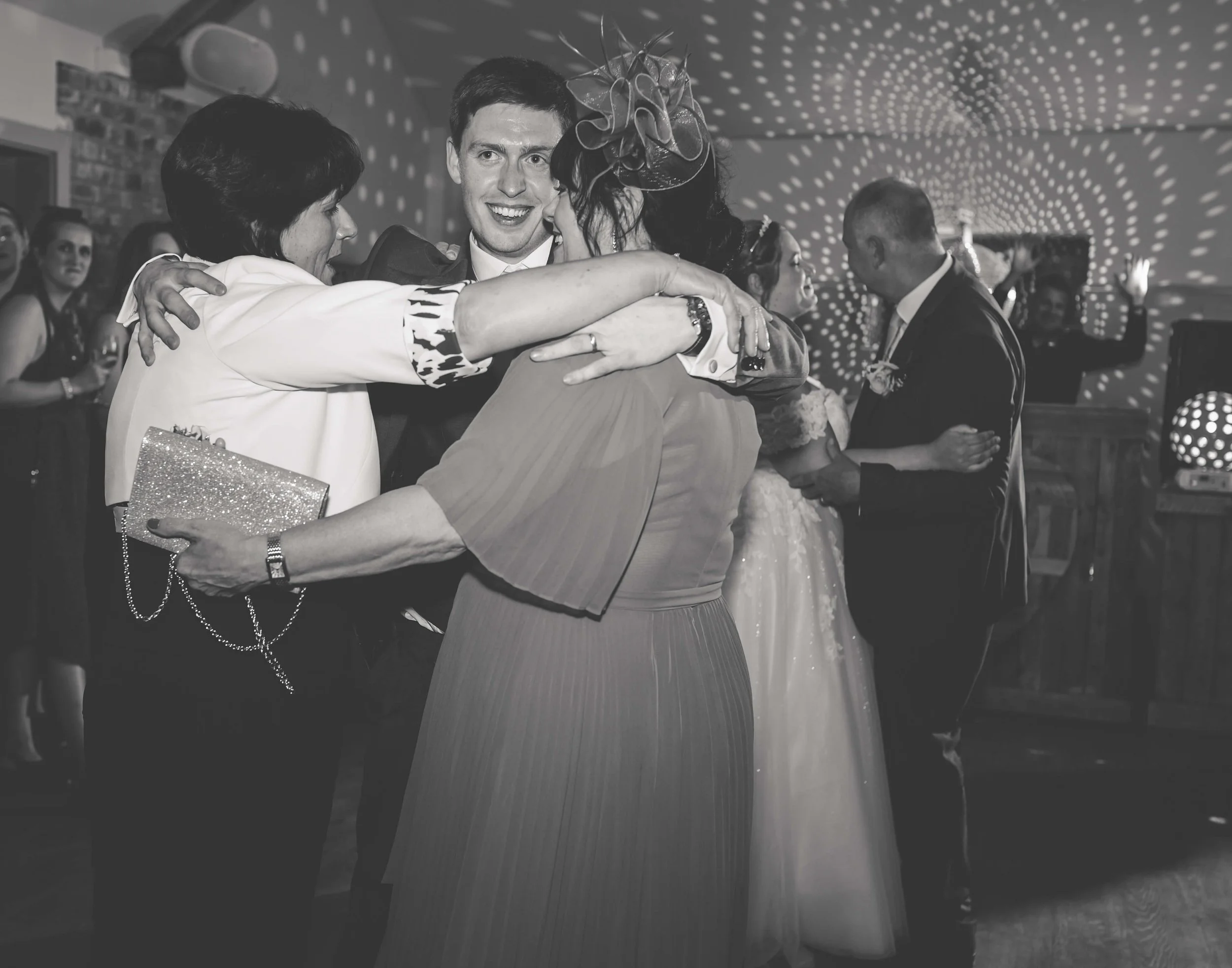 People dancing and hugging at a wedding reception with disco lights overhead, black and white photo.