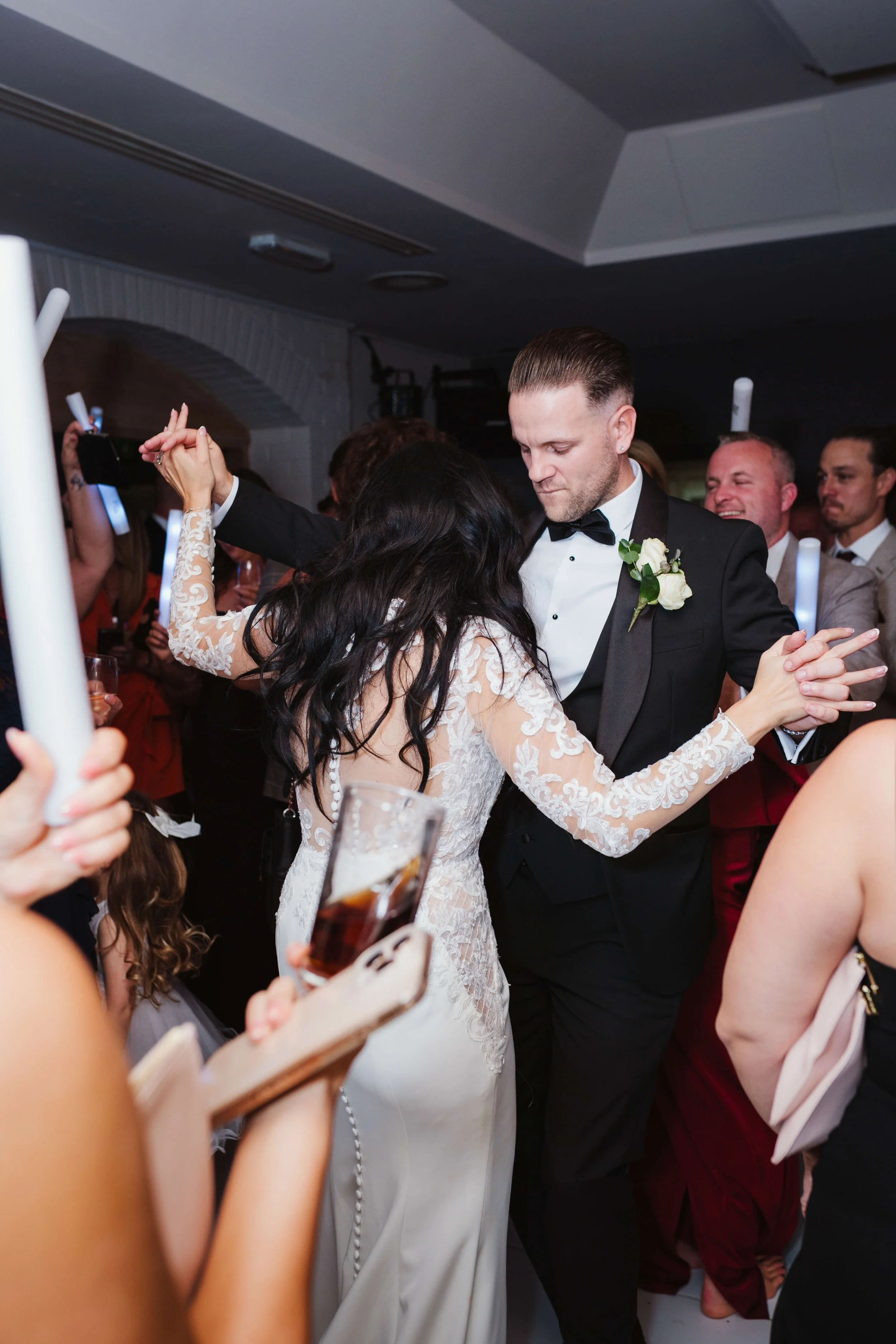 A bride and groom dance together at their wedding reception, surrounded by guests, in a dimly lit indoor venue.