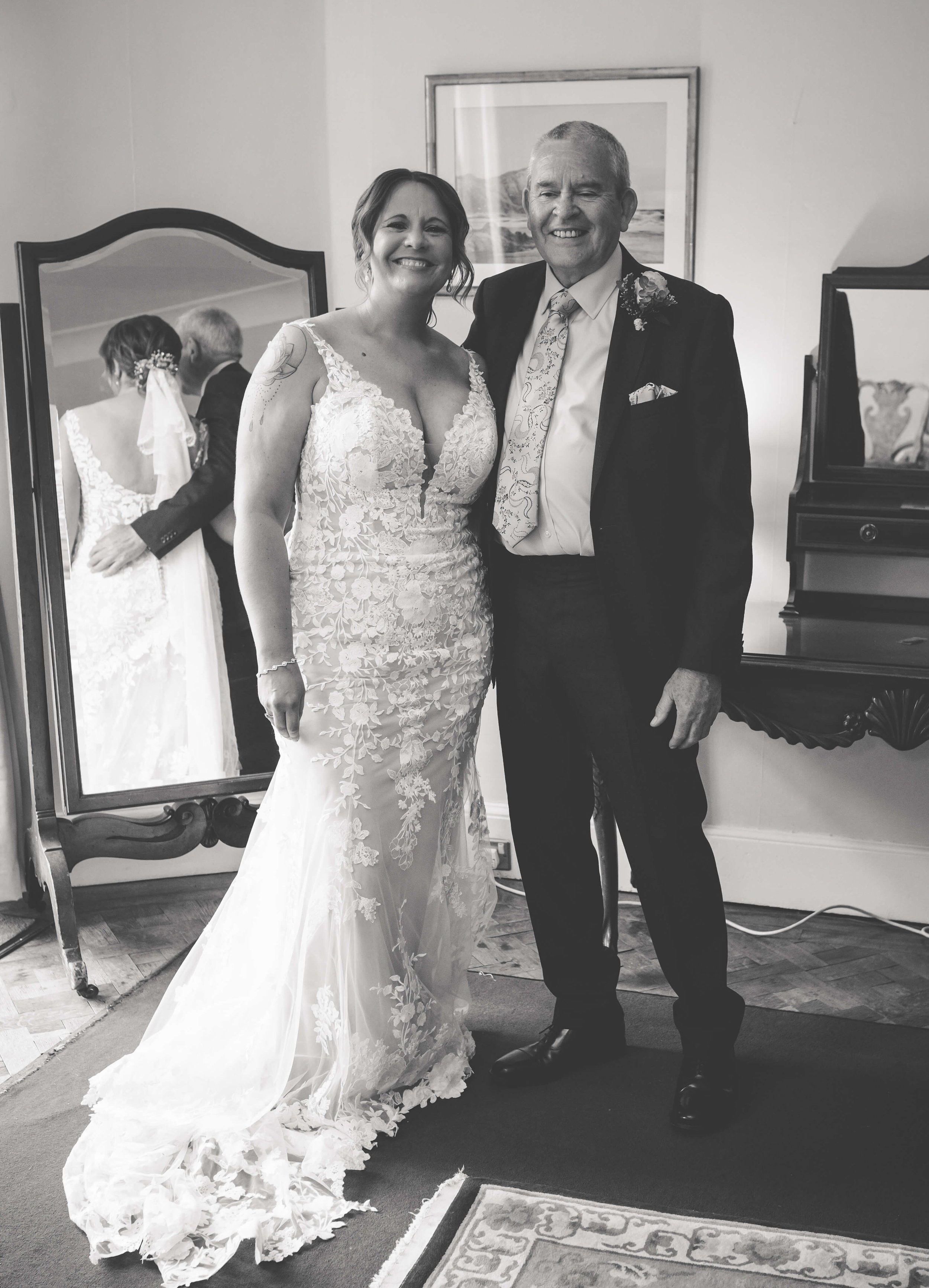 A bride and groom smiling and standing together after their wedding, reflected in a mirror behind them.