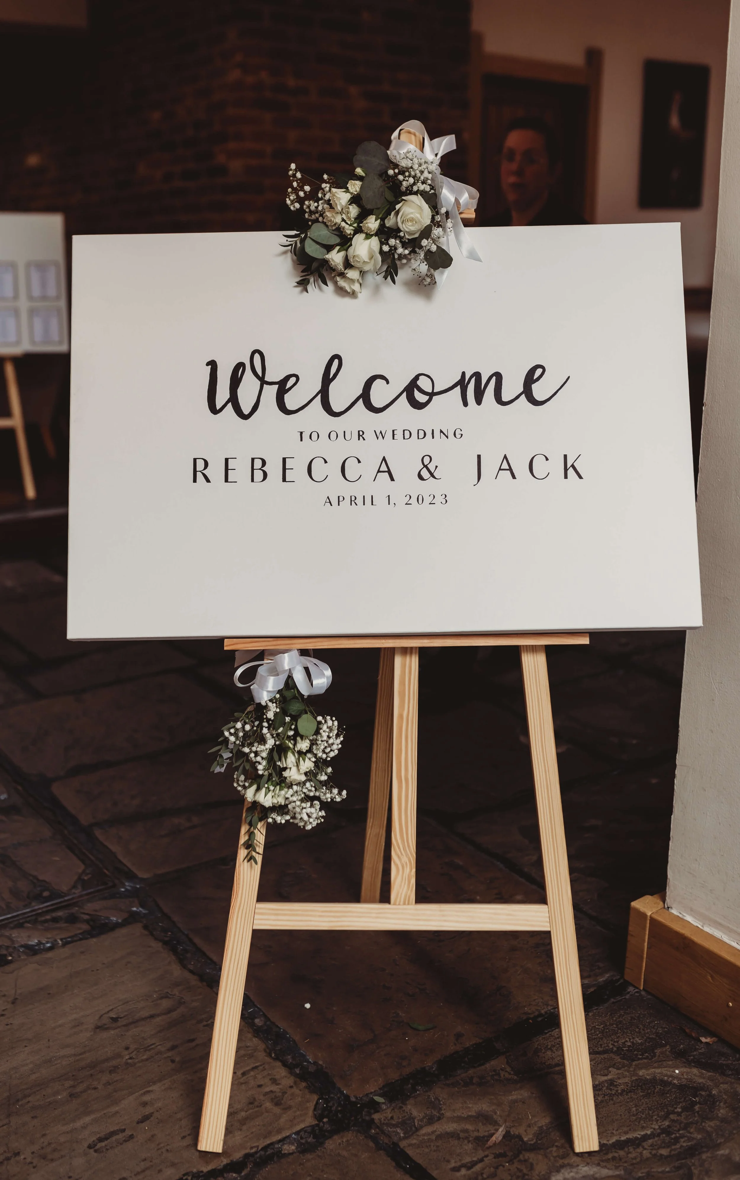 Welcome sign on an easel with flower decorations for Rebecca and Jack's wedding, dated April 1, 2023.