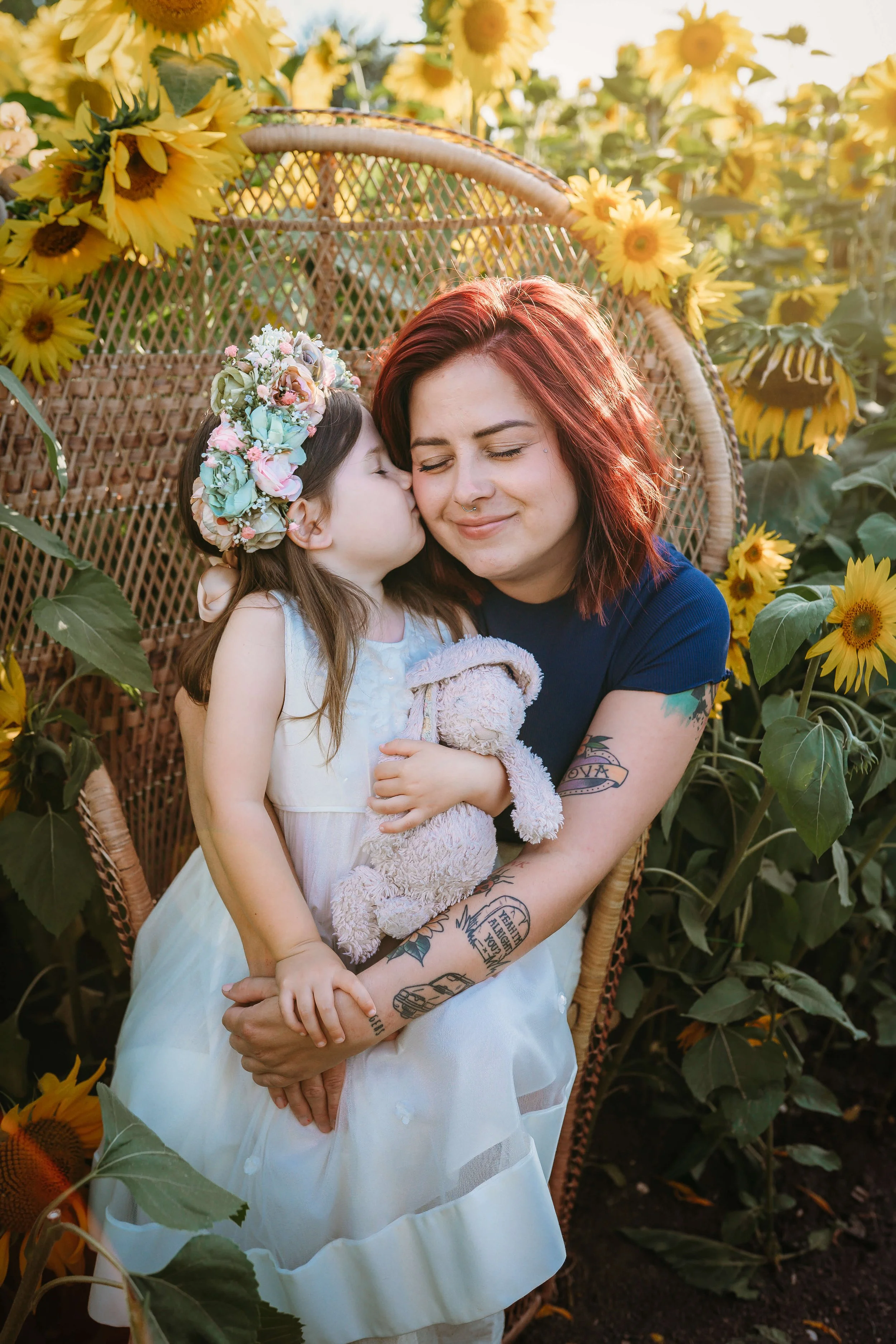 daughter kisses mum on peacock chair in sunflower field