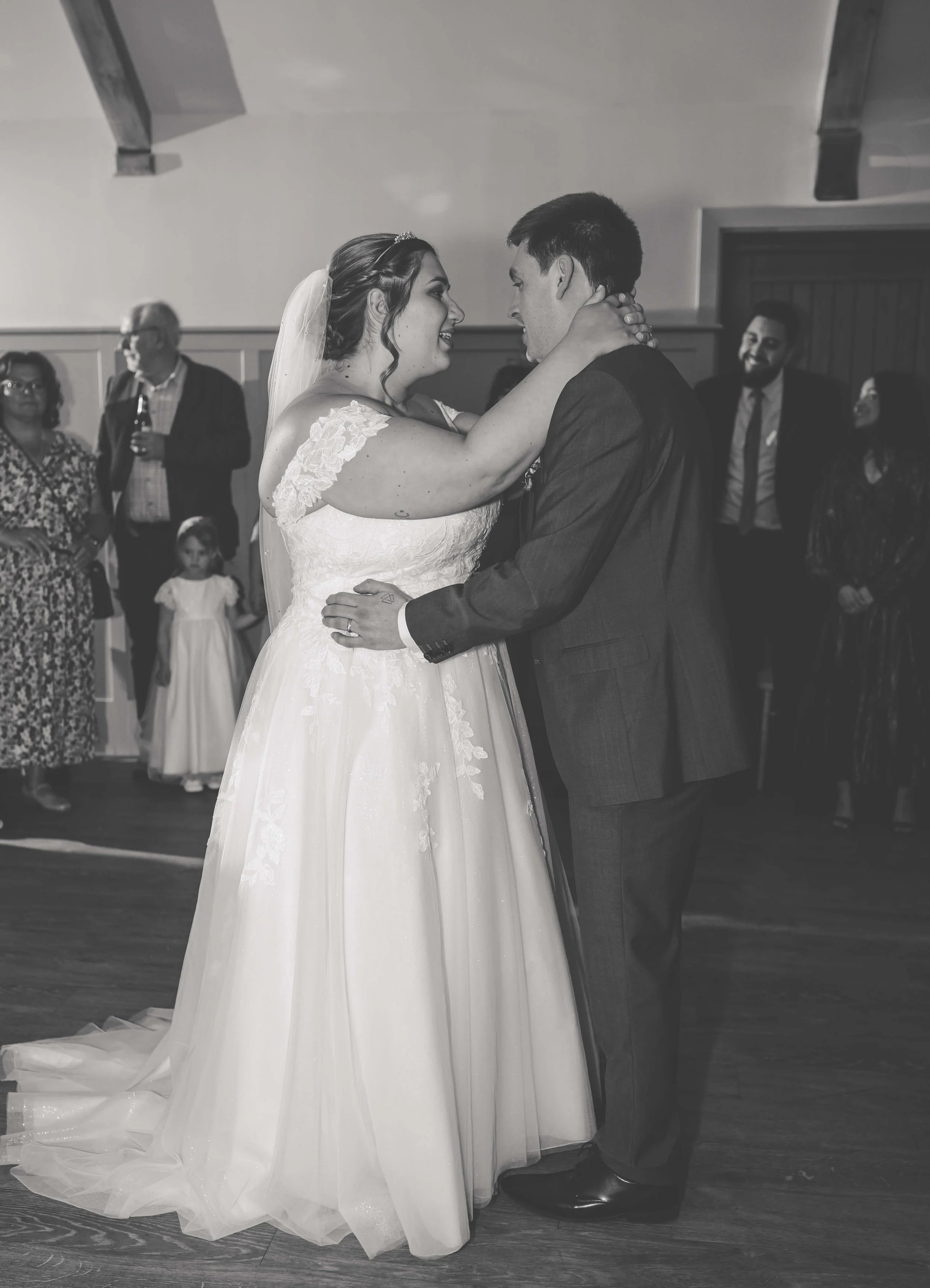 A bride and groom sharing a dance at their wedding reception with guests watching in the background.