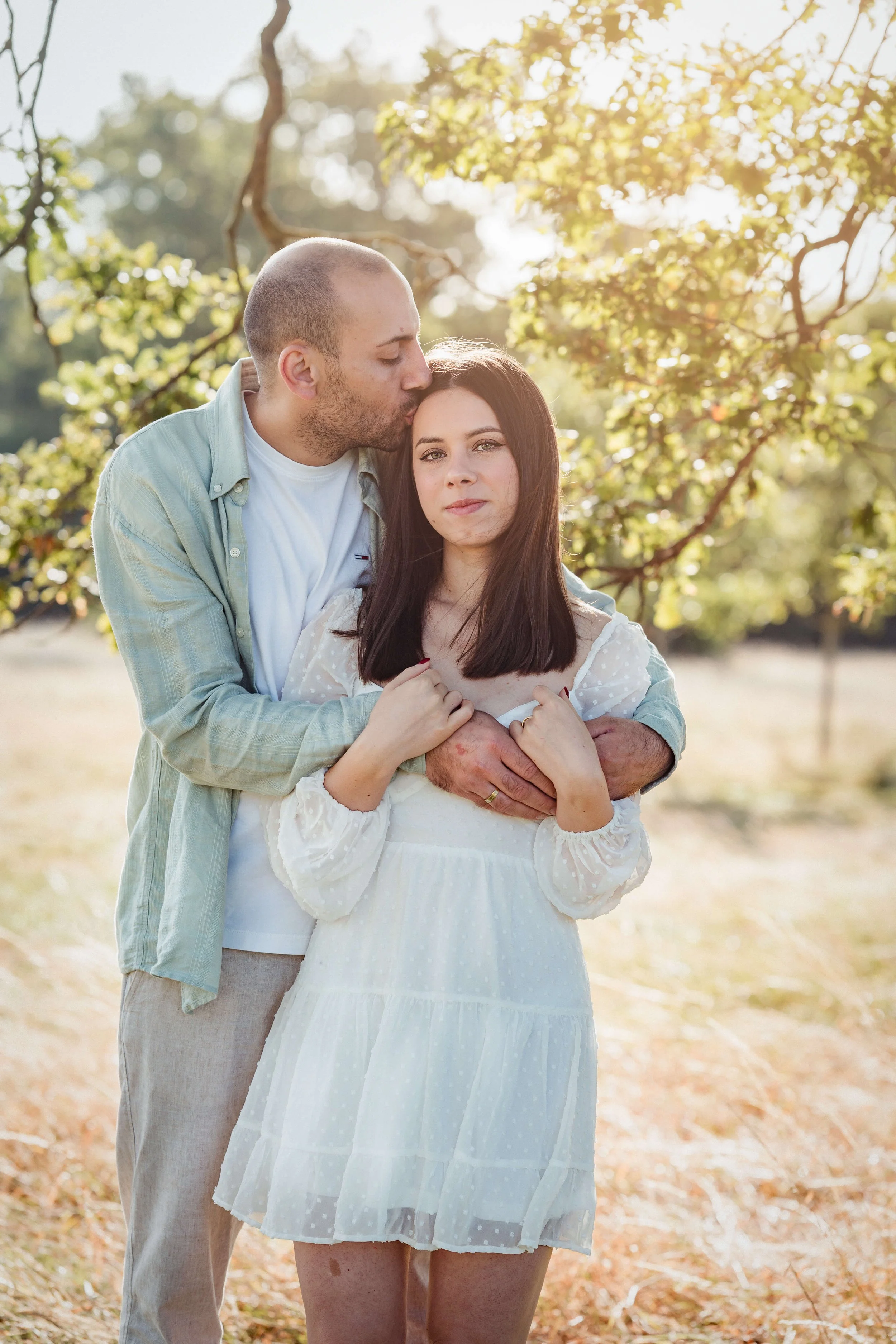 engaged couple in park man kisses head of fiancee