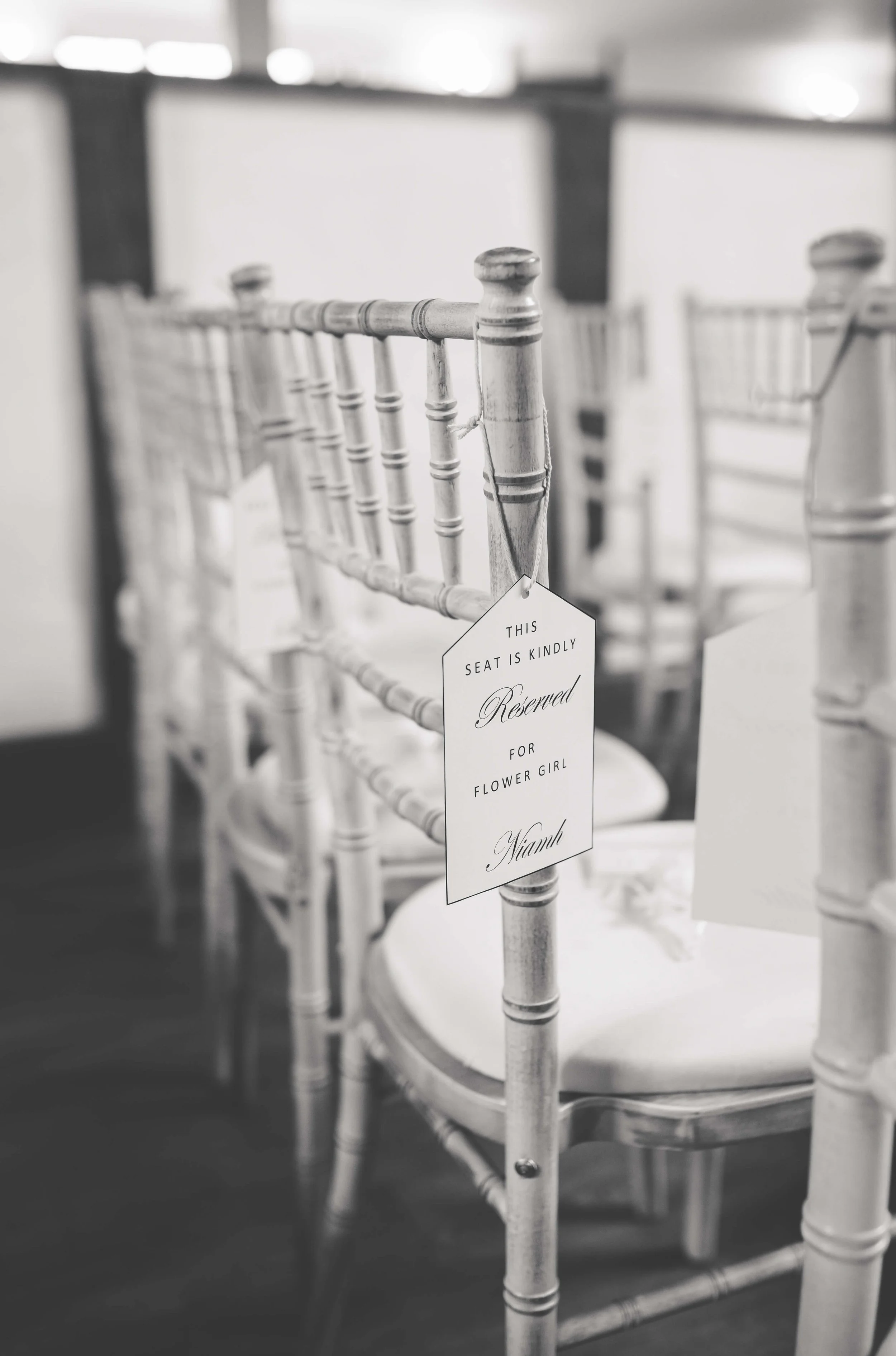 Row of white Chiavari chairs with reserved sign hanging, likely at a wedding or event.