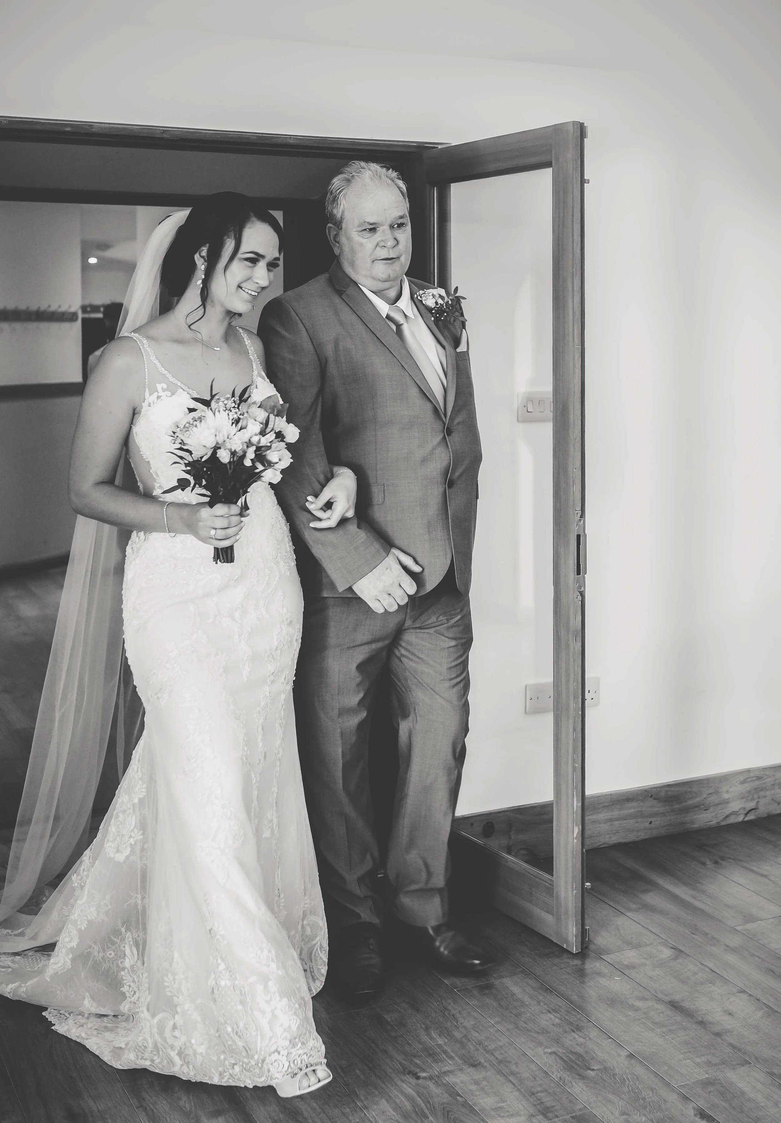 A bride in a white lace wedding dress holding a bouquet walking down the aisle with a man in a suit.