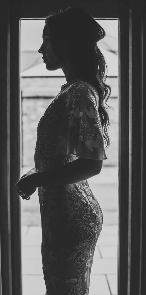 Silhouette of a woman standing near a window, wearing a patterned dress.
