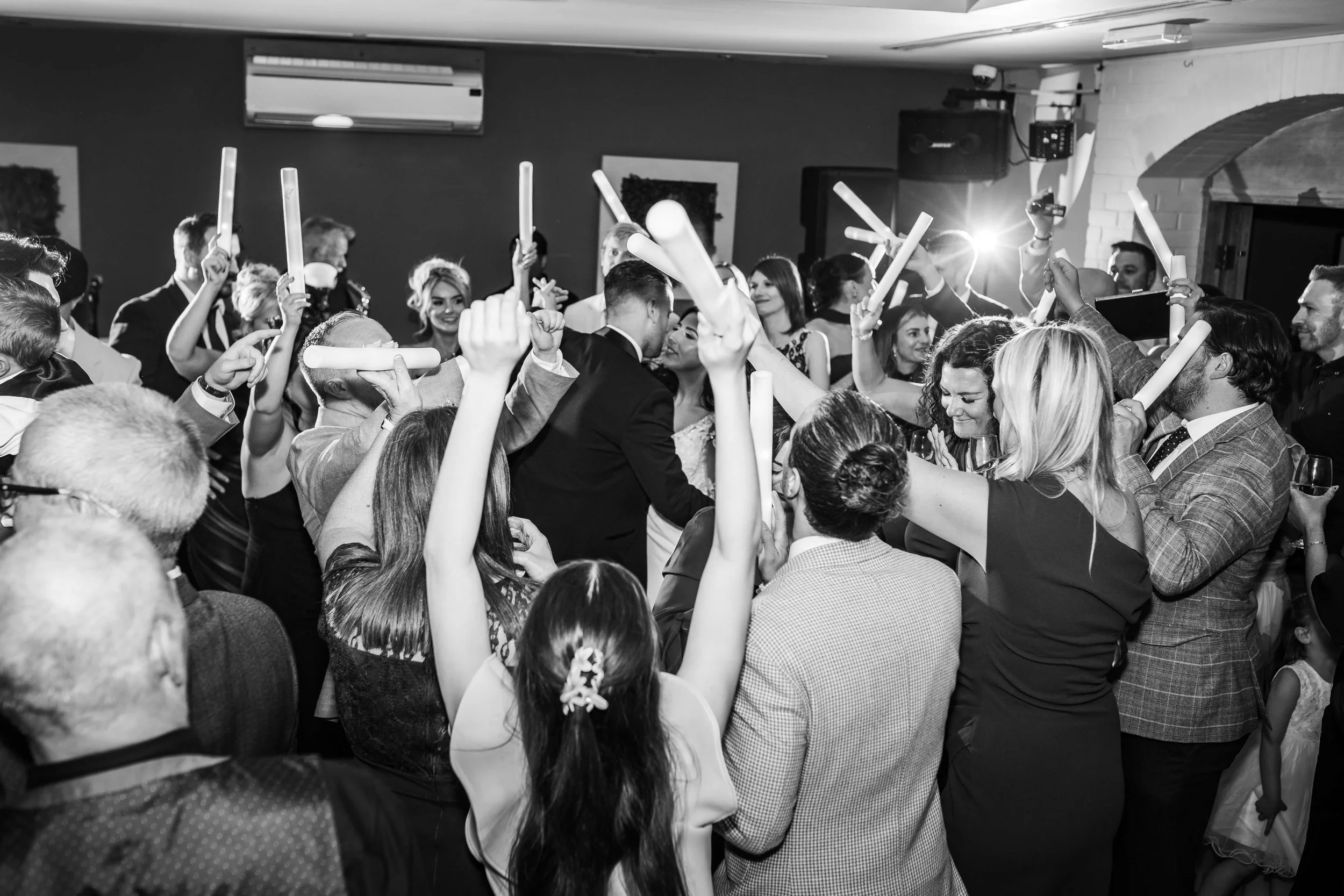 People celebrating at a party or wedding, raising glow sticks and enjoying under dim lighting.