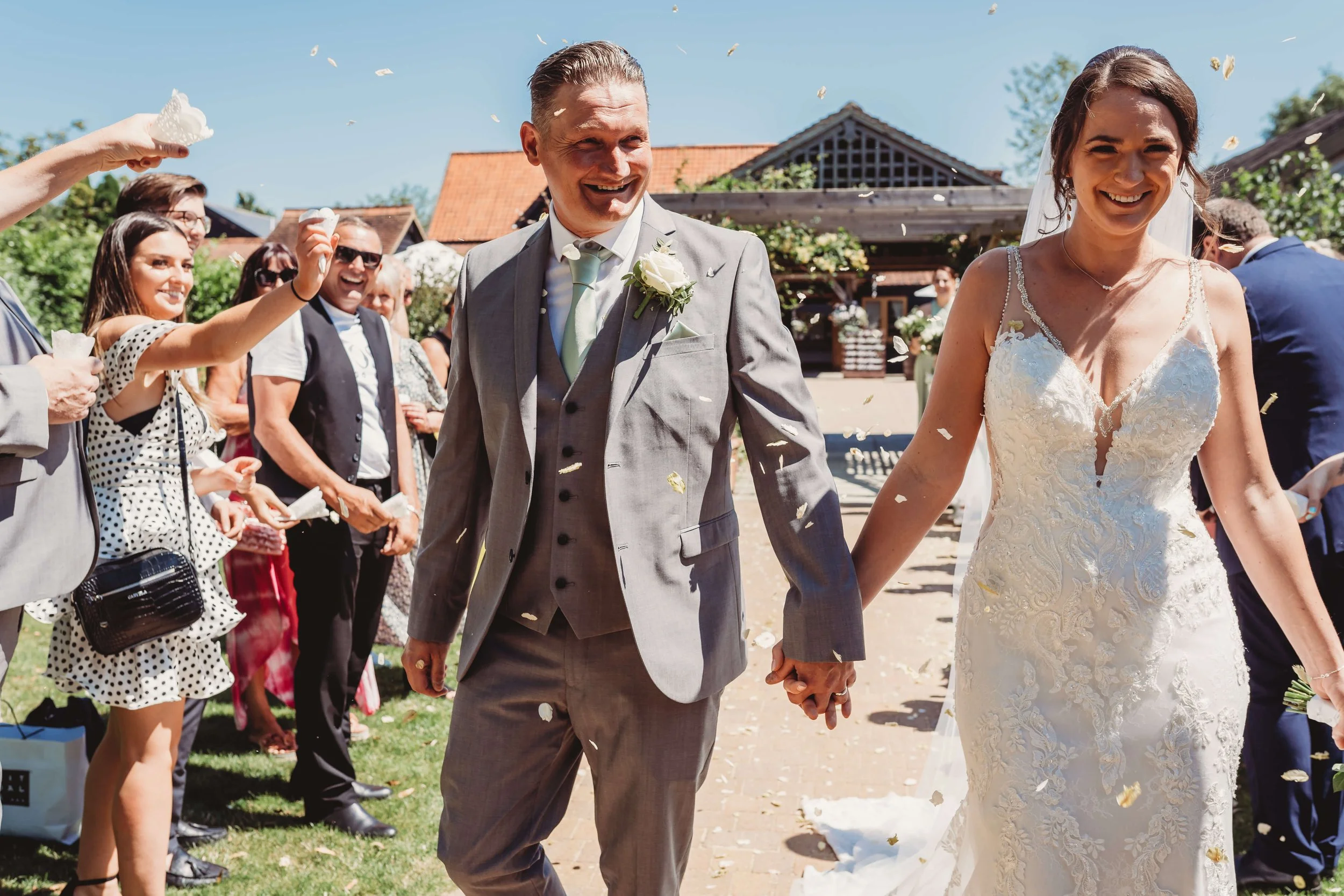 A bride and groom walking hand in hand away from wedding guests who are throwing rice or confetti during their outdoor wedding celebration.