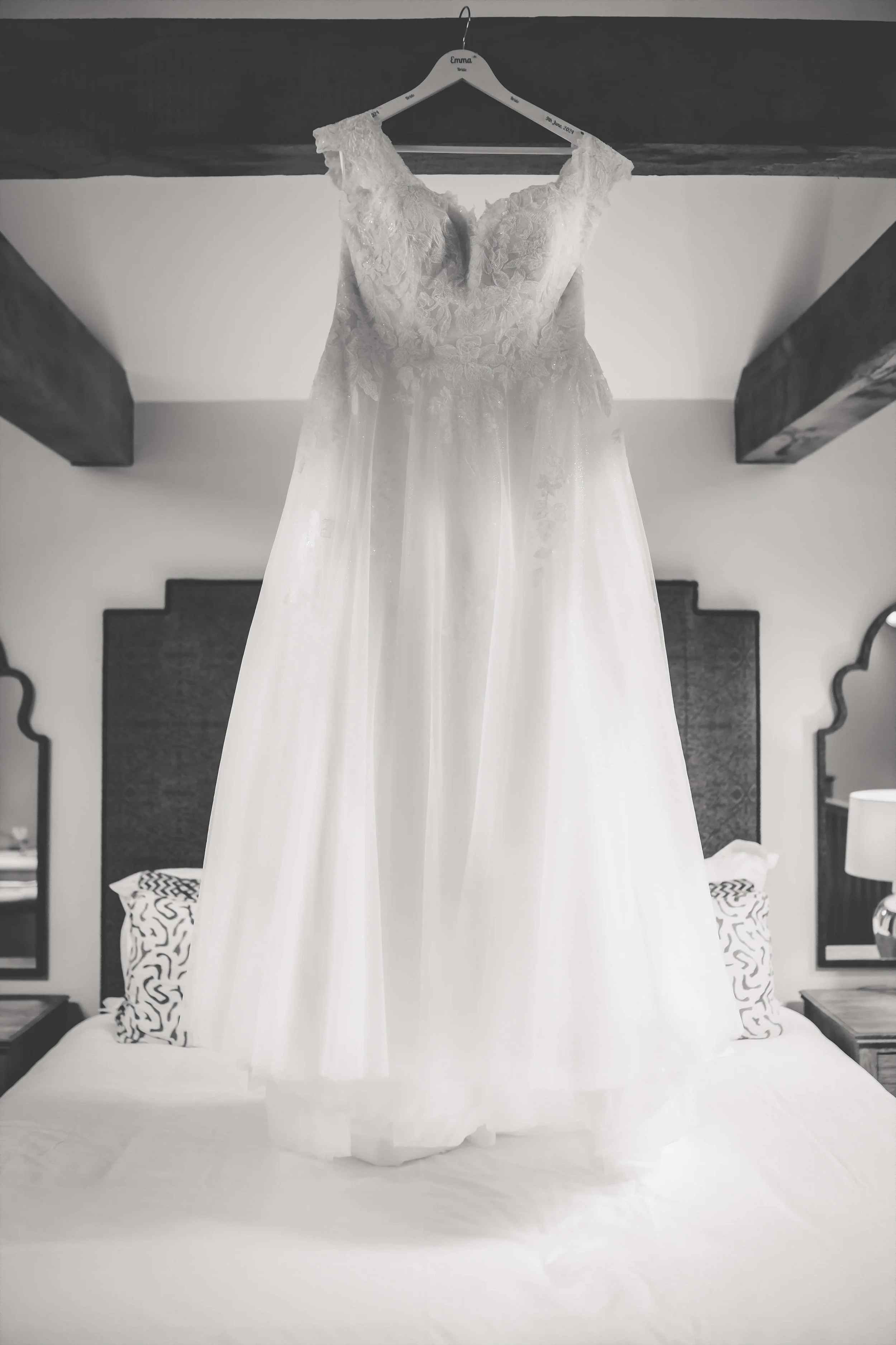 A white wedding dress hanging on a hanger over a bed.