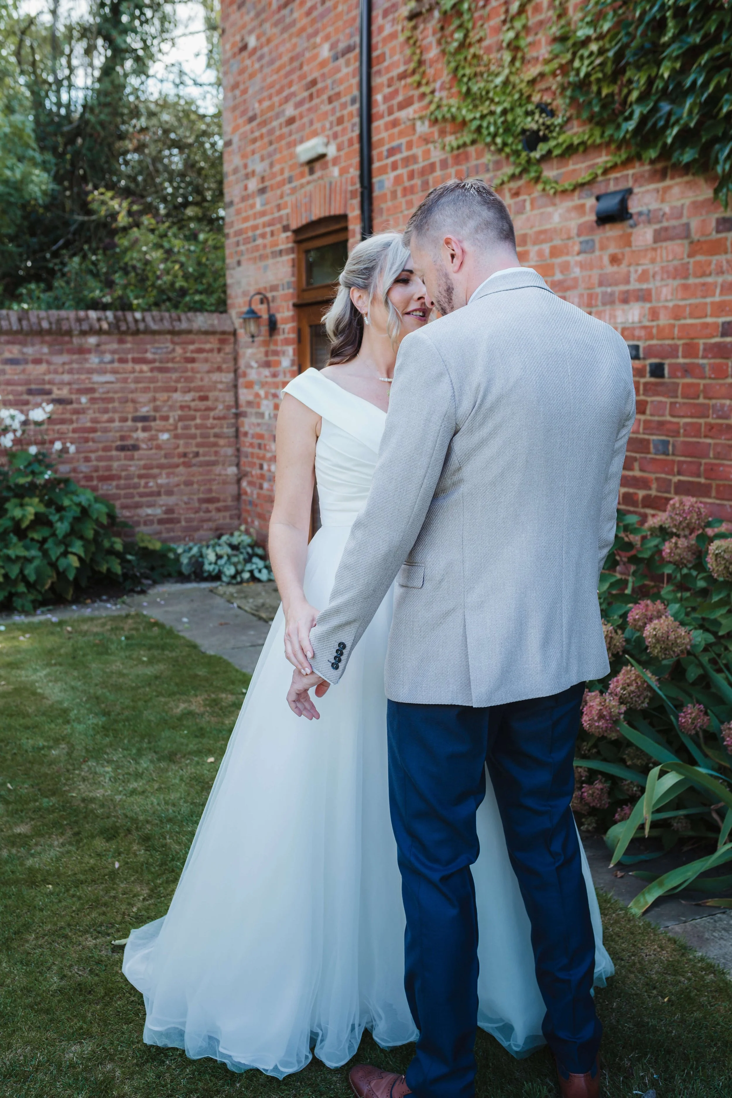 A bride and groom holding hands and touching foreheads outside in a garden during their wedding.