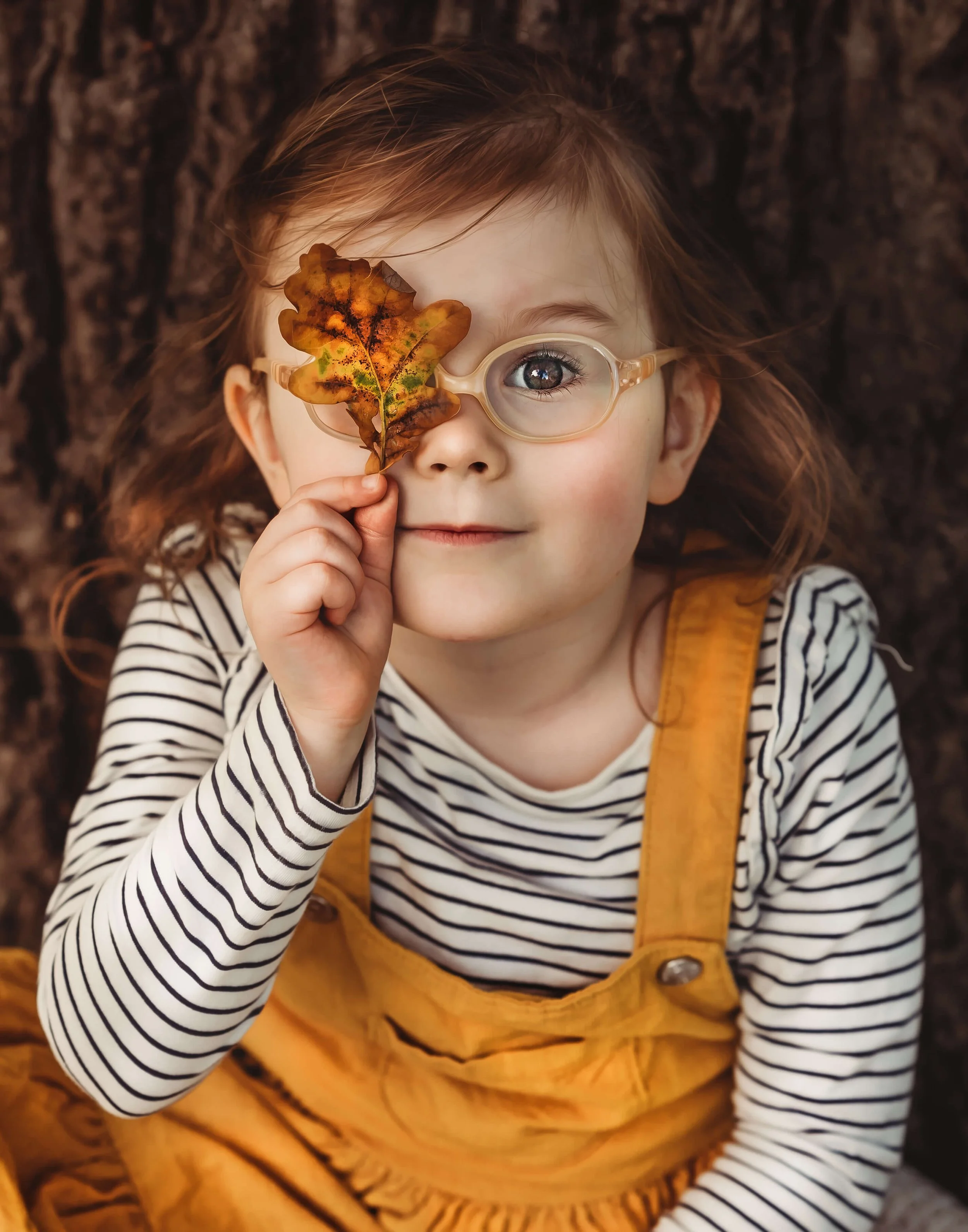 girl in autumnal clothing with leaf over her eye posing for a photo in a woodland themed photo session