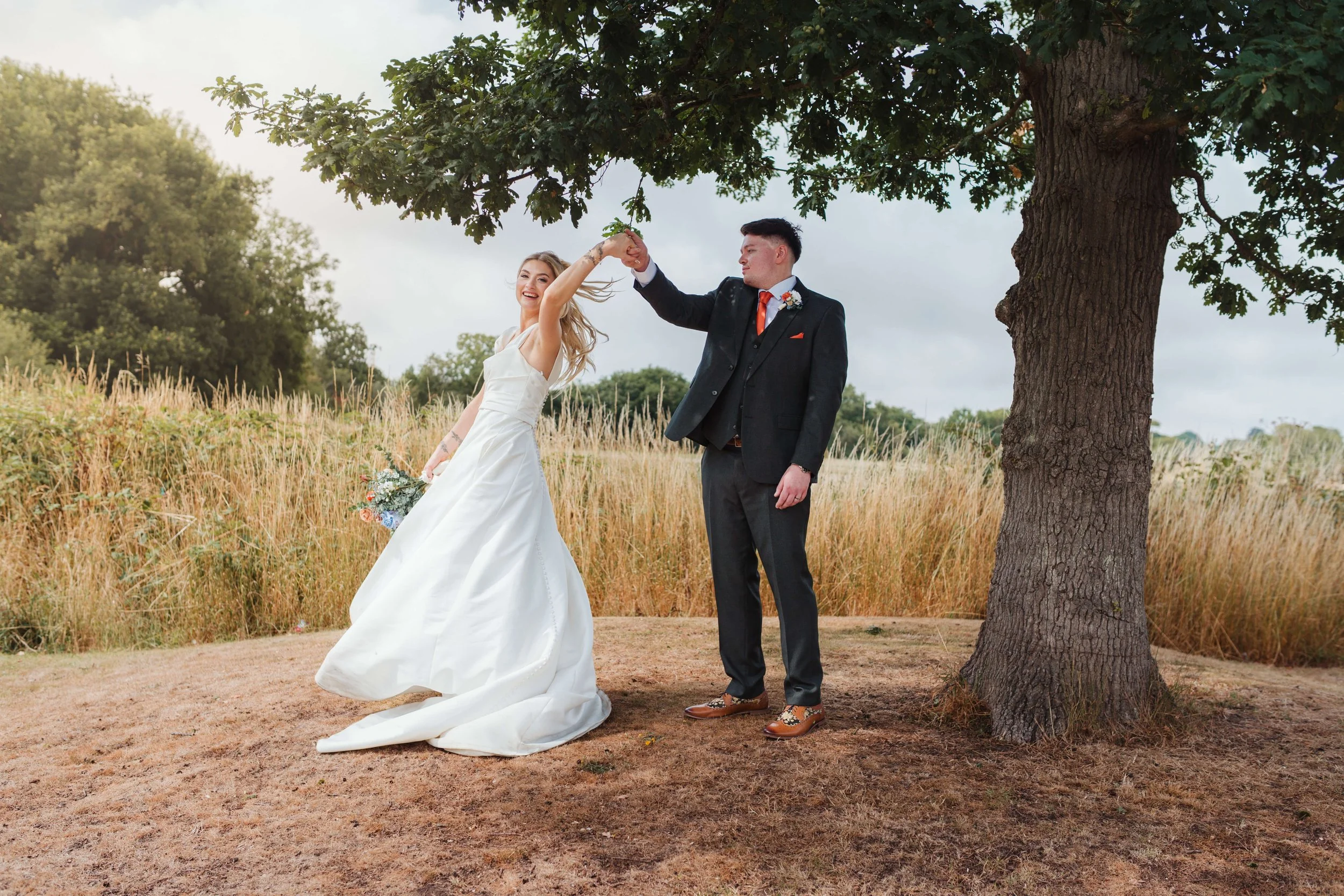 groom twirling the bride under a tree 