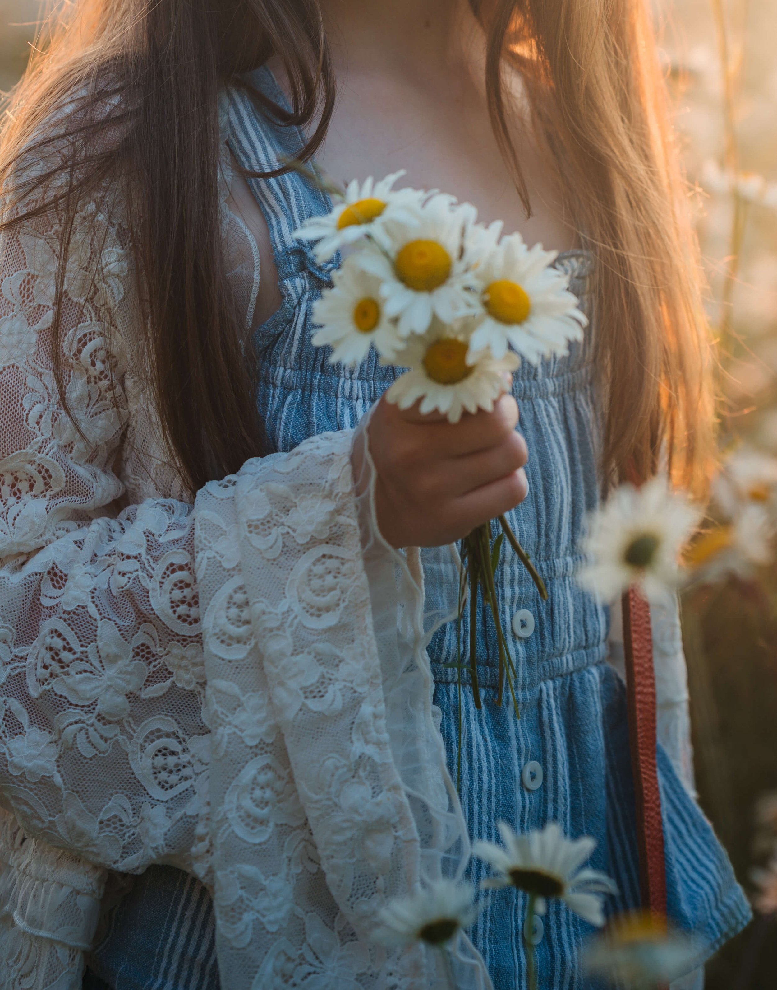 Person holding a bouquet of daisies outdoors at sunset.