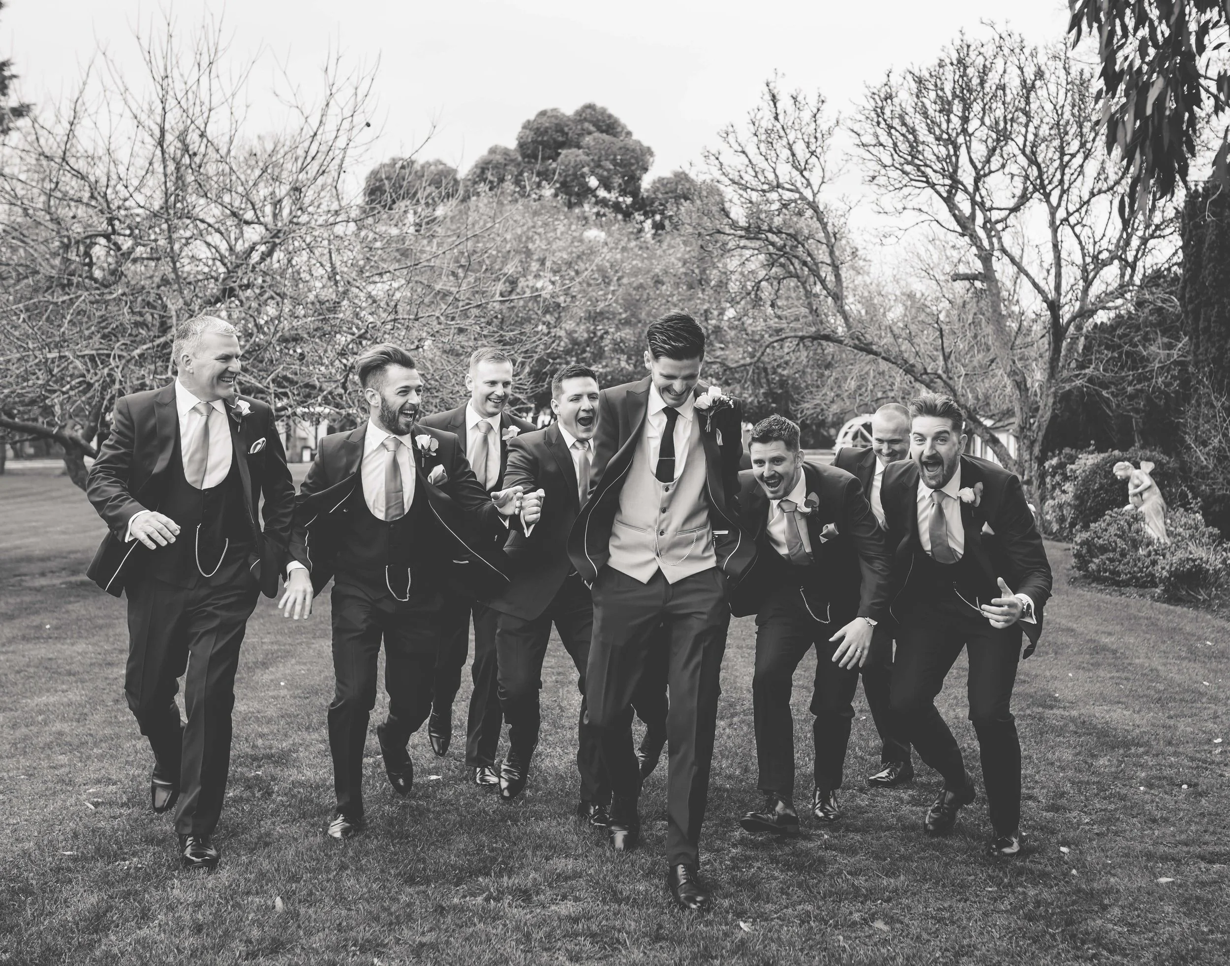groomsmen running after groom in black and white photo