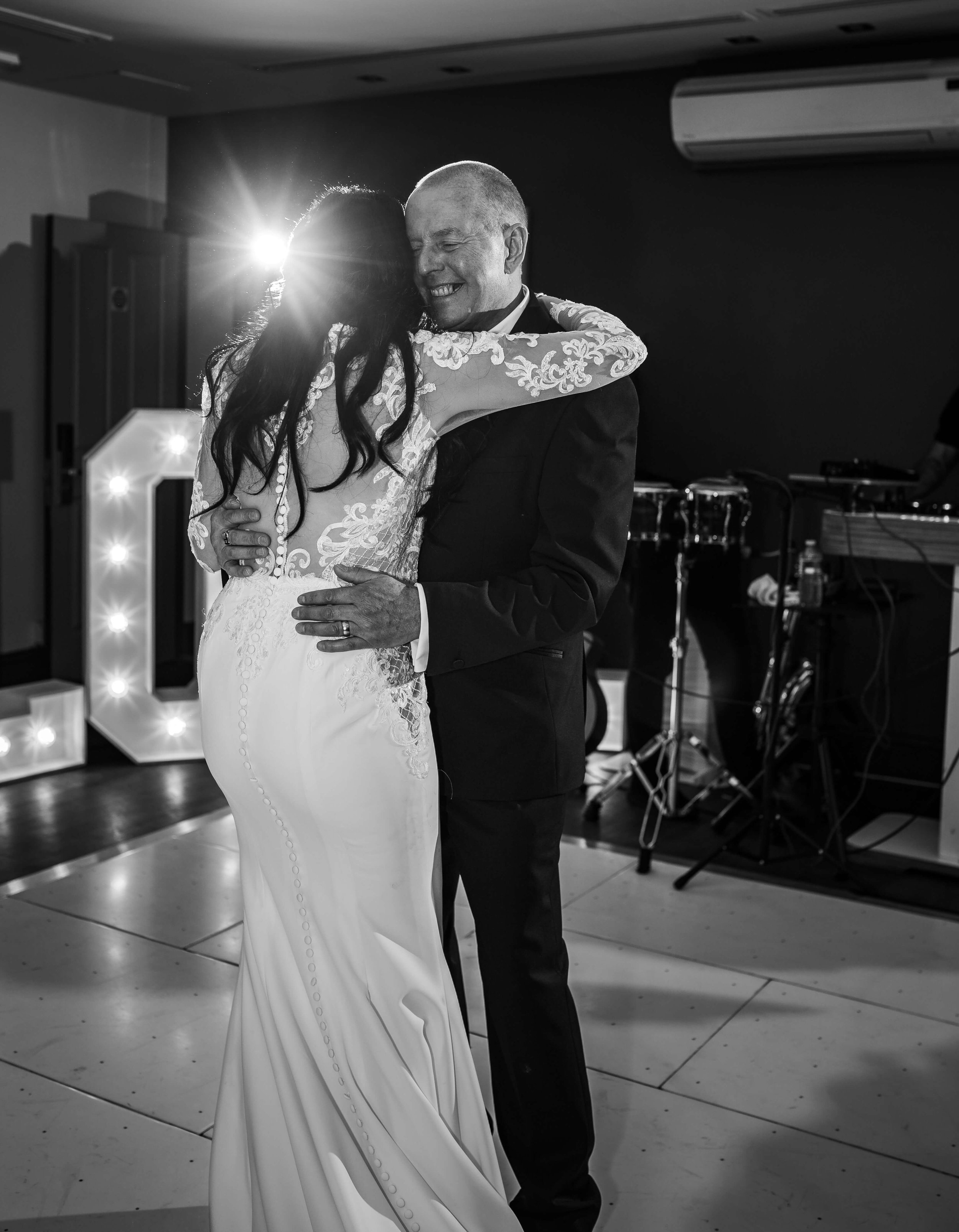 A bride and groom sharing their first dance at a wedding reception, with a large illuminated letter 'D' in the background.