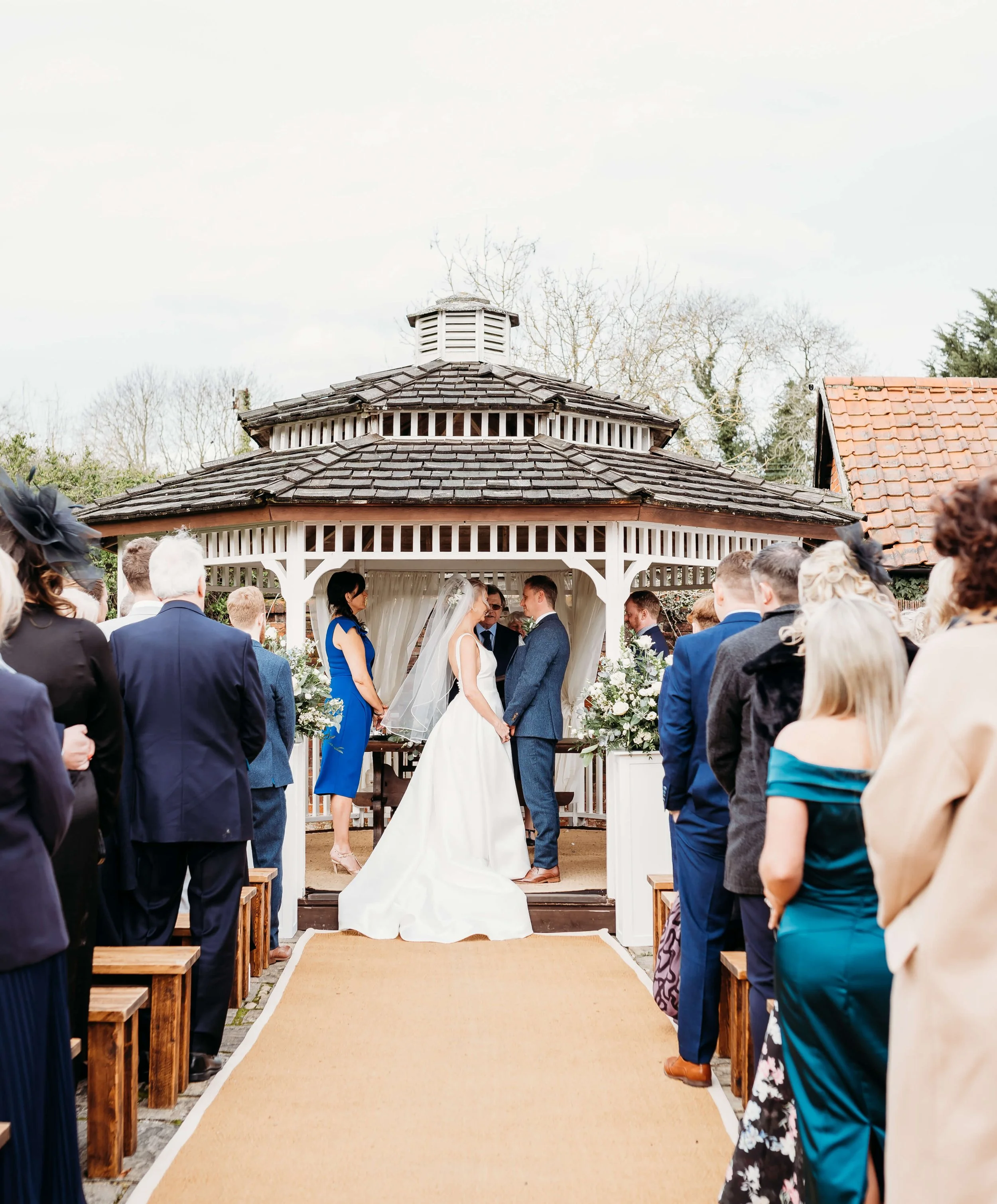 A wedding ceremony taking place outdoors under a gazebo with participants and guests.