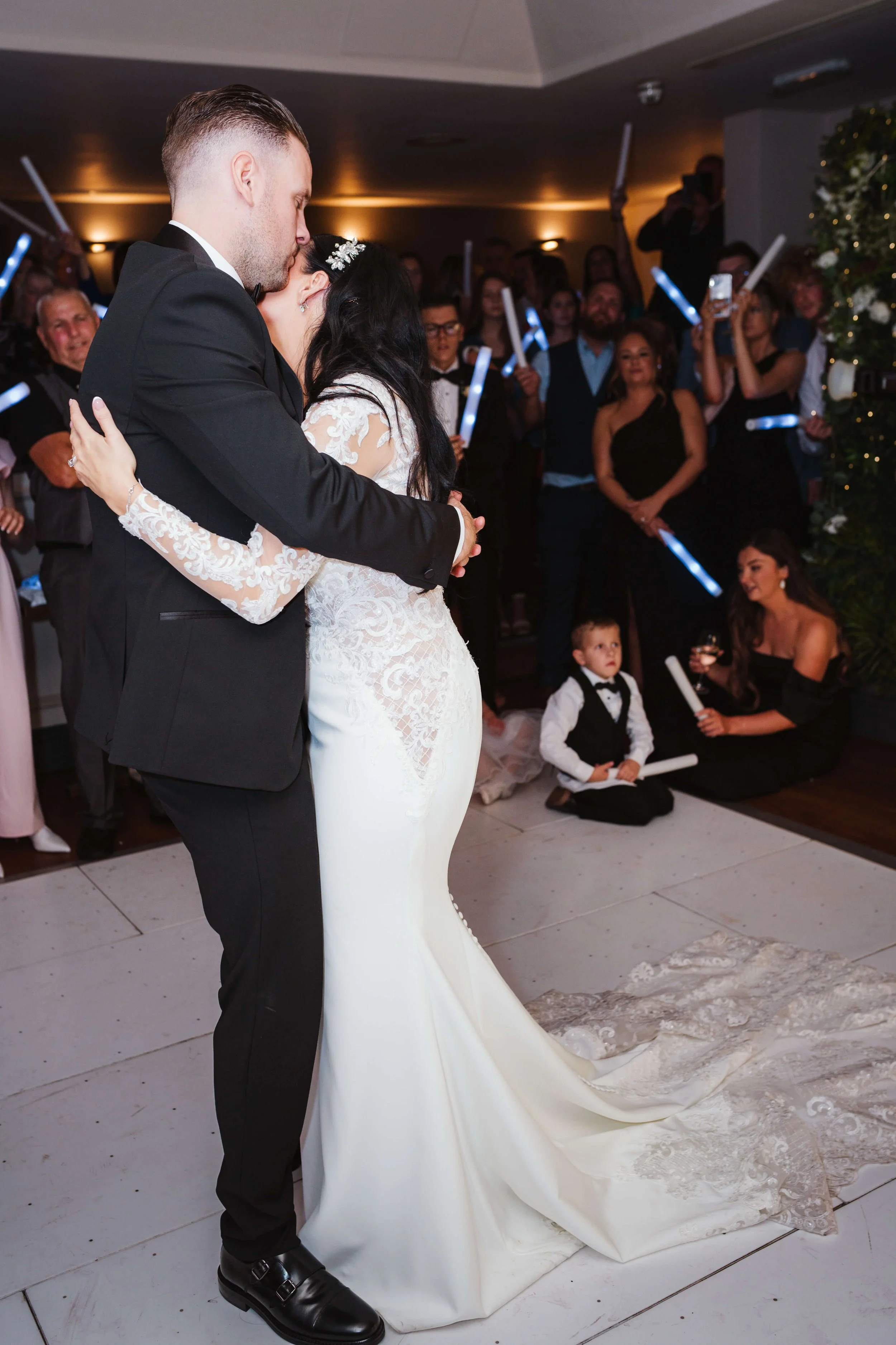A newlywed couple sharing a first dance at their wedding reception, surrounded by friends and family.