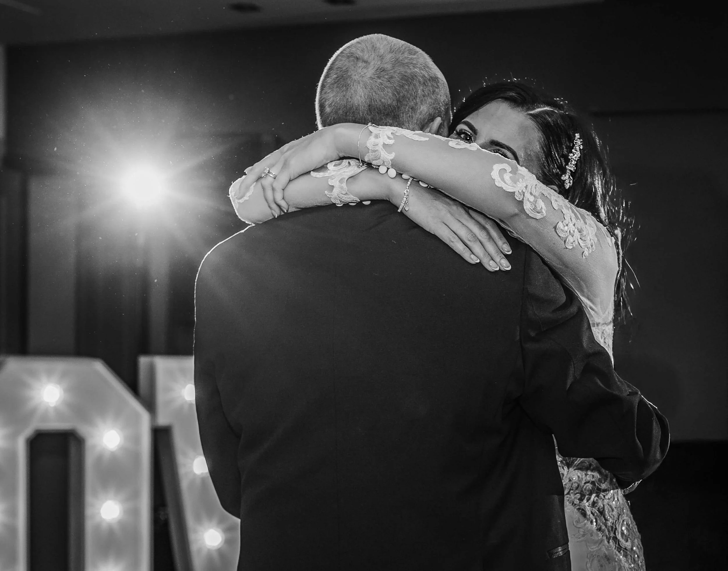 A black and white photo of a bride and groom sharing a first dance, hugging closely, with the bride's face visible and smiling.