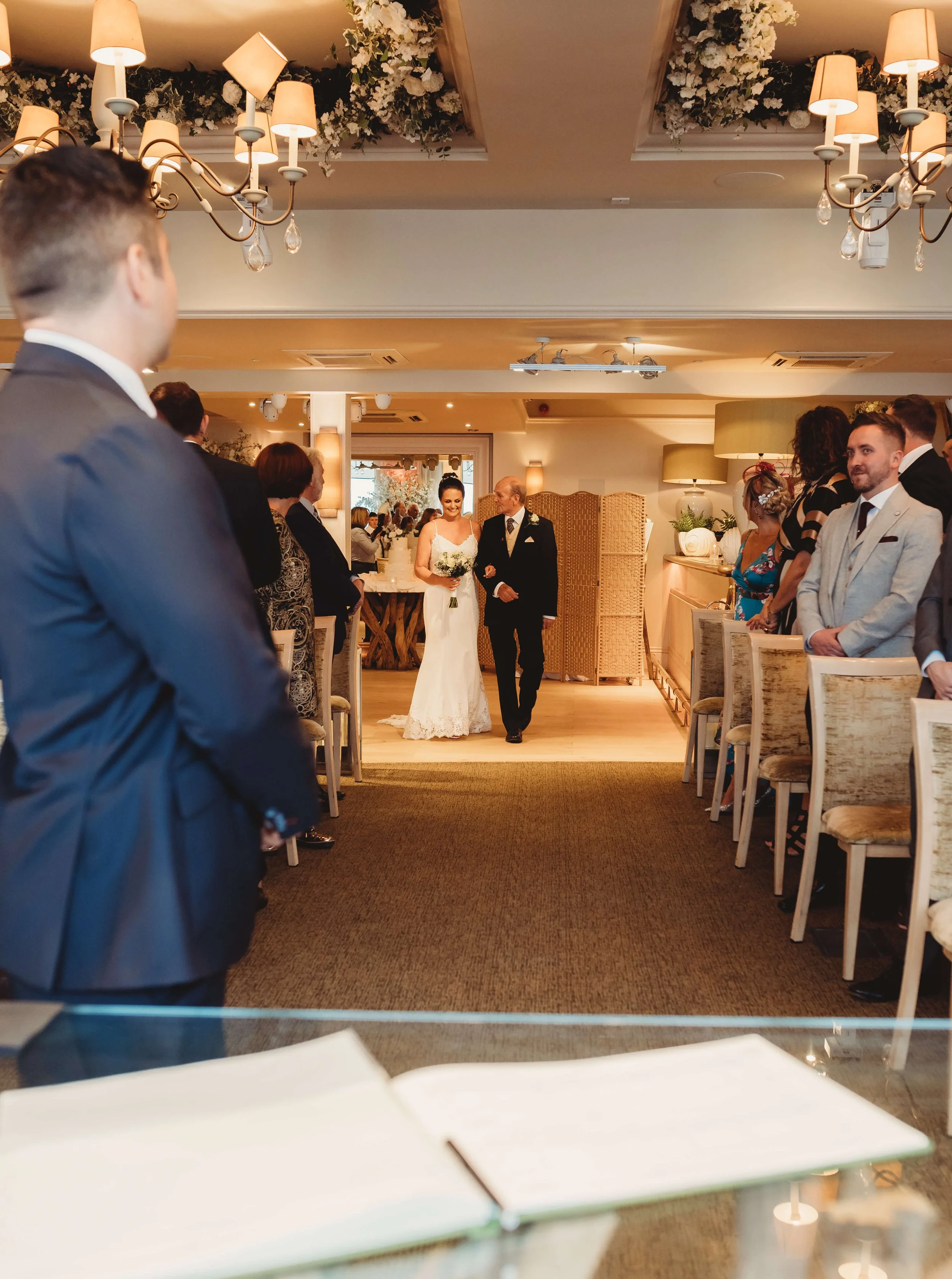 A bride walking down the aisle with her escort at a wedding ceremony in a decorated indoor venue.