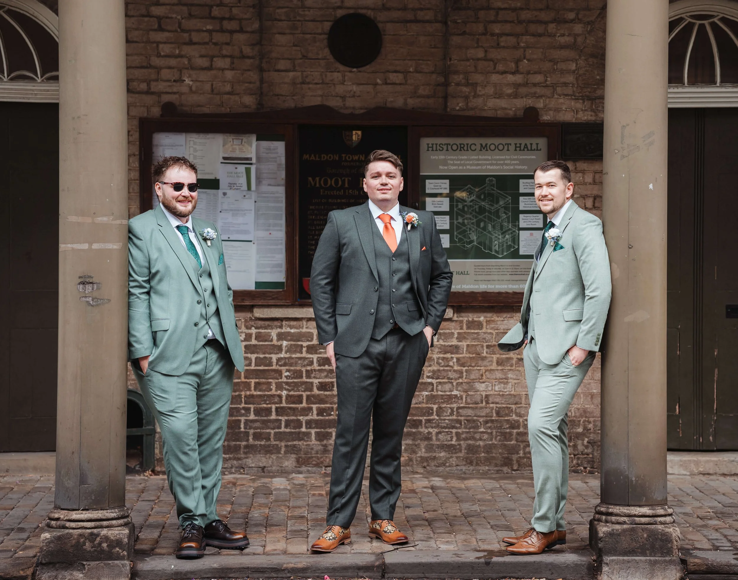 Three men in suits standing outside a brick building with a sign that reads 'Historic Moot Hall'.