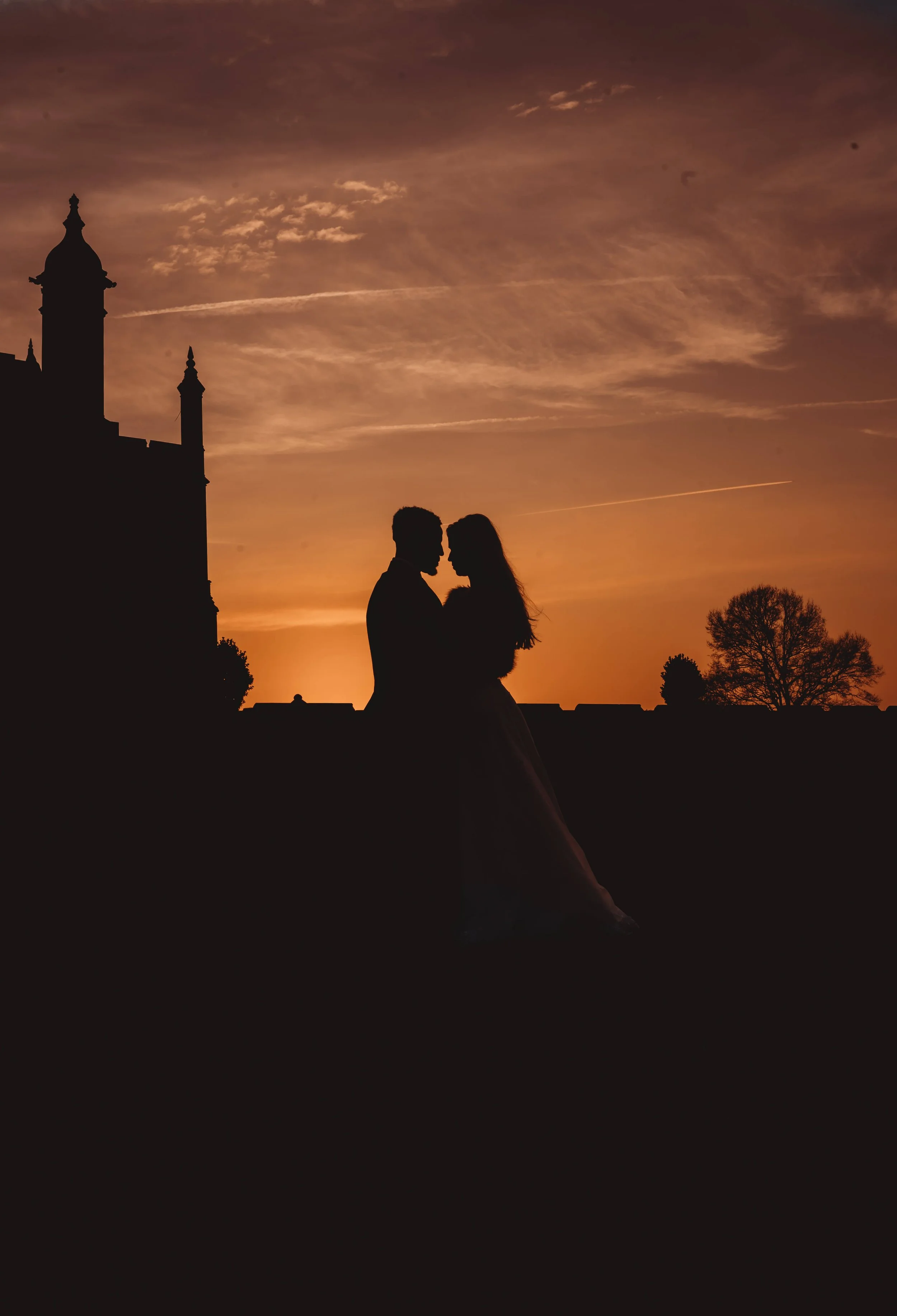Silhouette of a couple dancing outdoors during sunset with a castle and trees in the background.