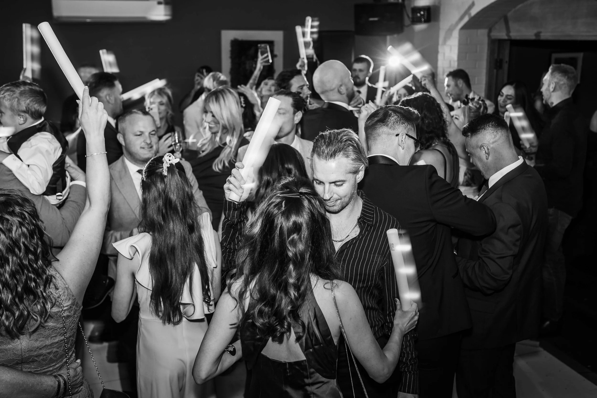 People dancing and socializing at a party, holding glow sticks in a lively atmosphere.