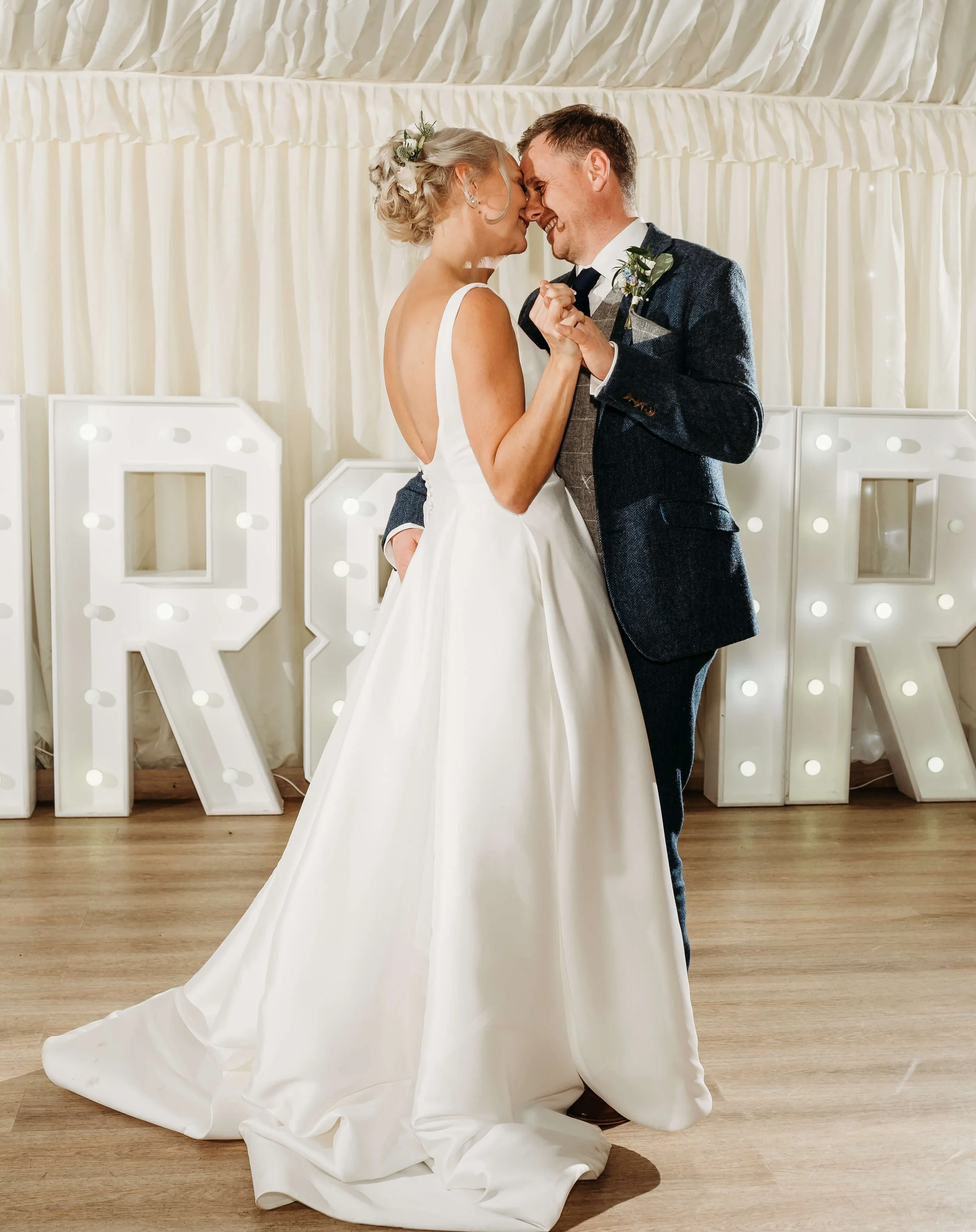 Bride and groom dancing closely at their wedding reception, with large illuminated letters in the background.