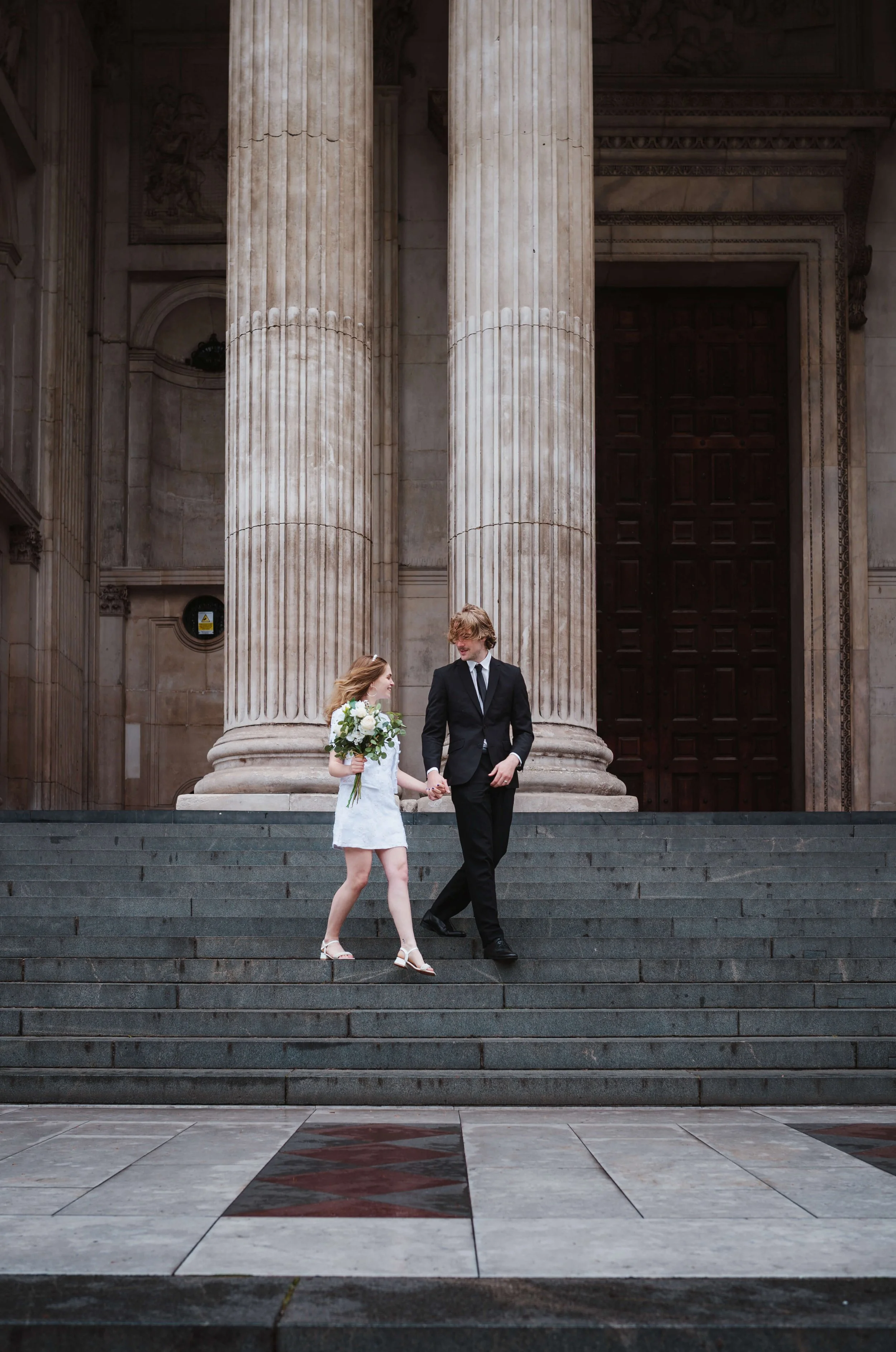 bride and groom walking along steps of St Pauls Cathedral 