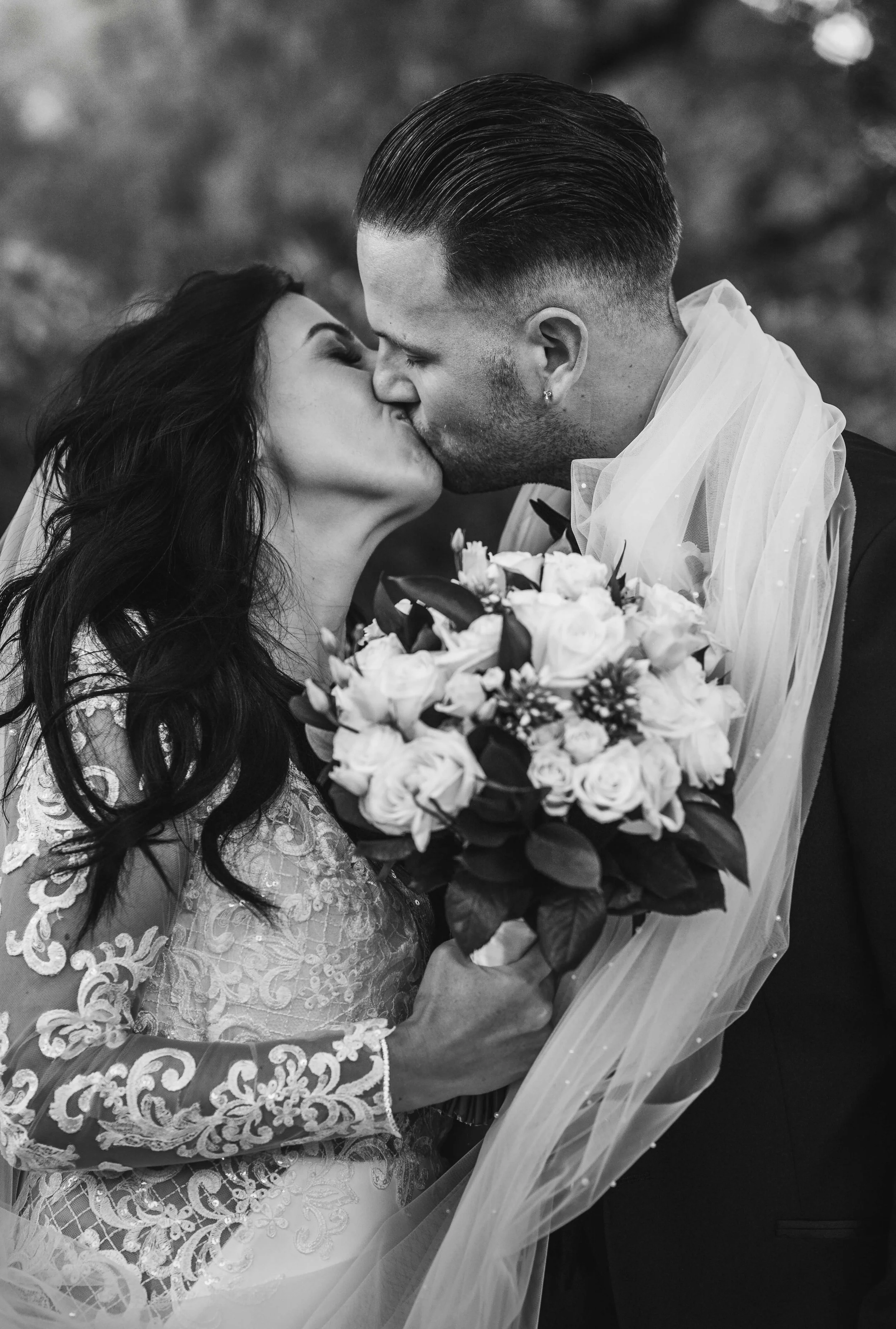 A black and white photo of a bride and groom kissing, with the bride holding a large bouquet of flowers.
