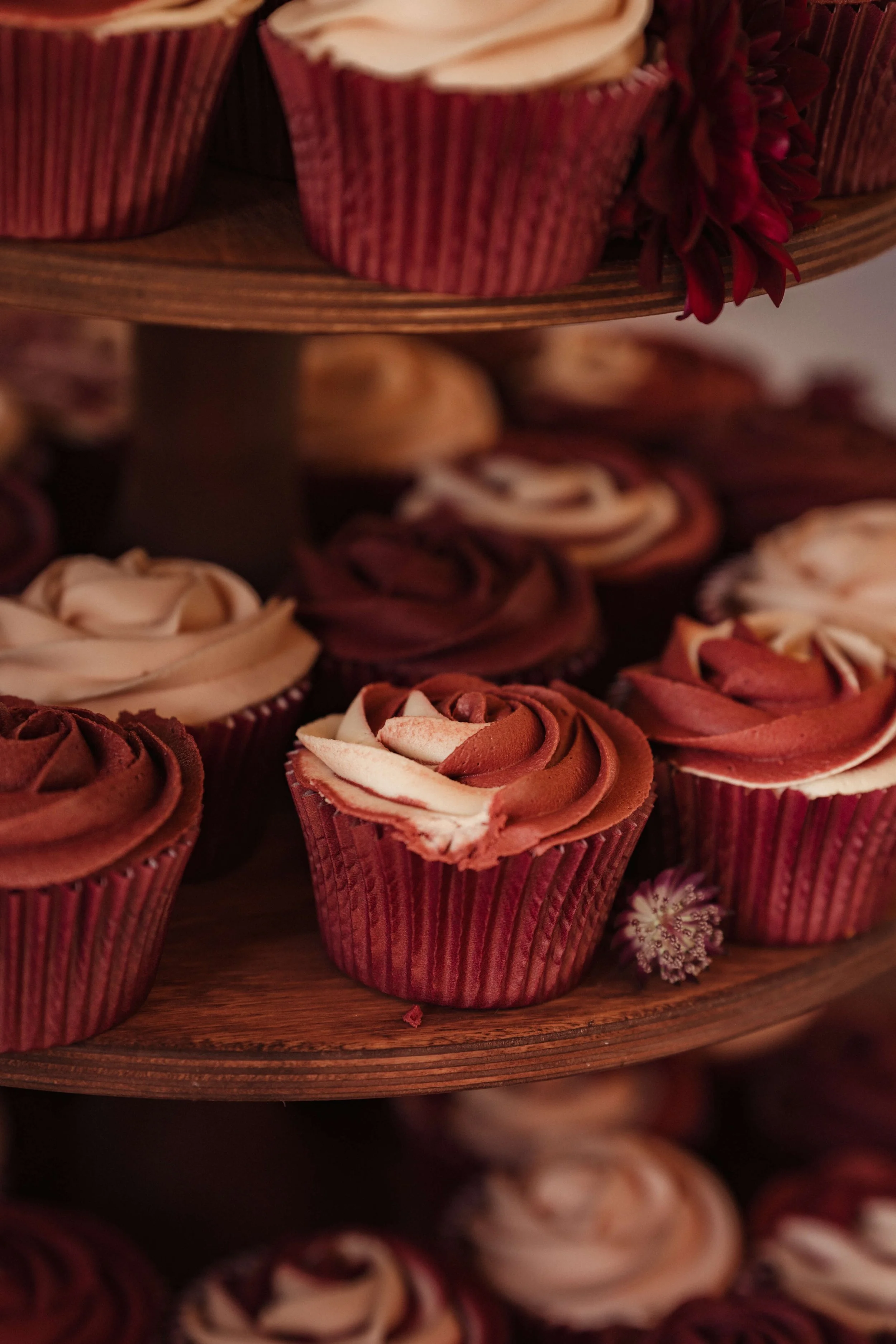 Close-up of chocolate and vanilla frosted cupcakes on a multi-tiered wooden stand, decorated with small purple flowers.