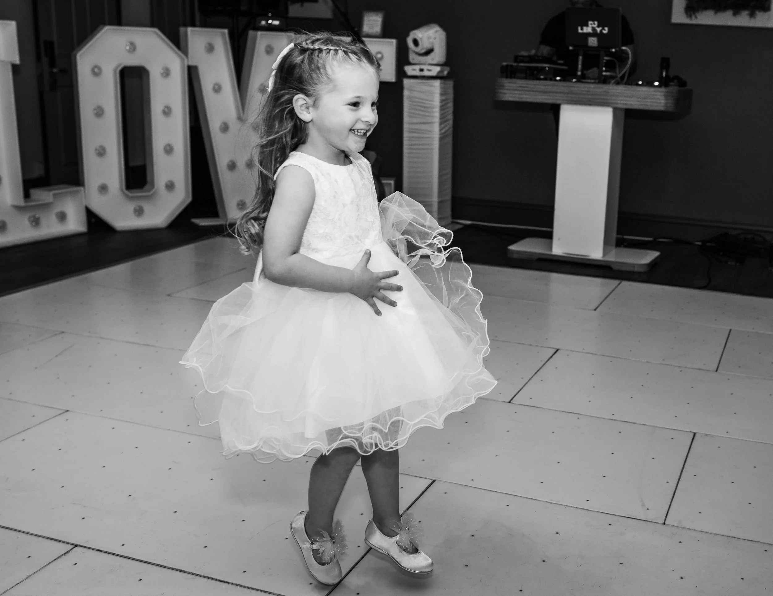 A young girl in a fancy dress smiling and dancing on a dance floor at a celebration event.