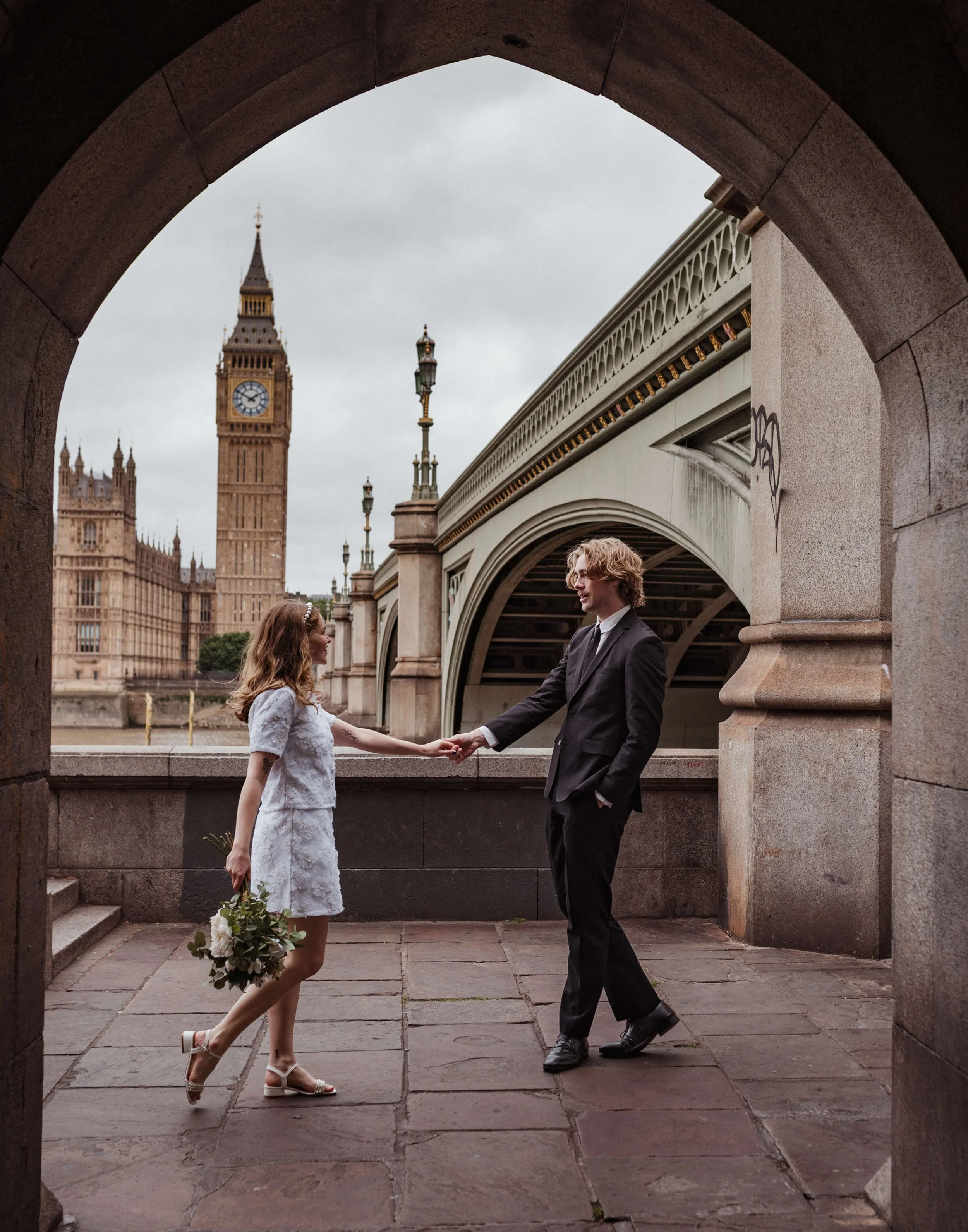 bride and groom hold hands and look into each others eyes whilst standing on the Southbank London opposite Big Ben, London Elopement