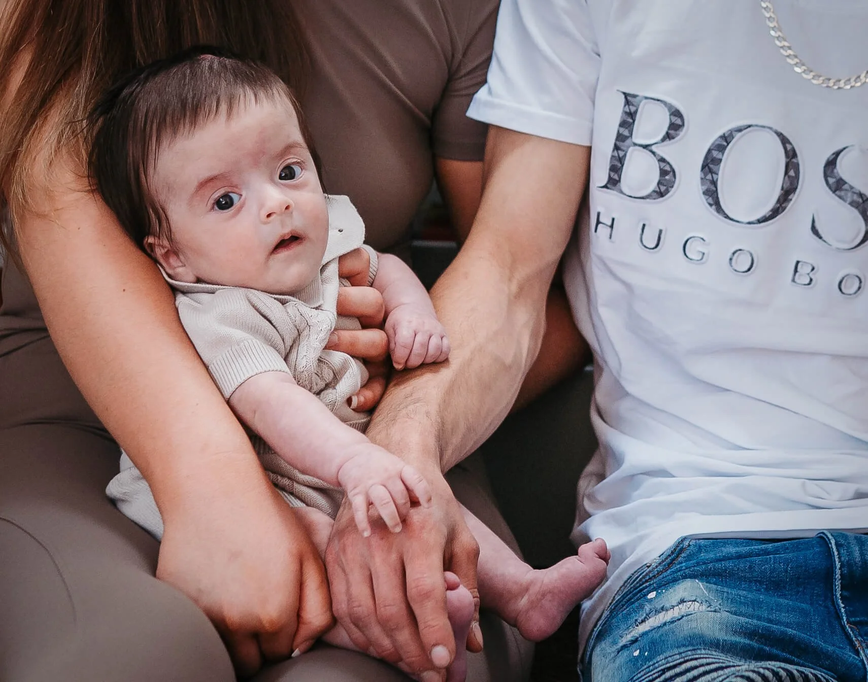 baby with lots of hair in his parents arms photo focuses on their hands and baby 