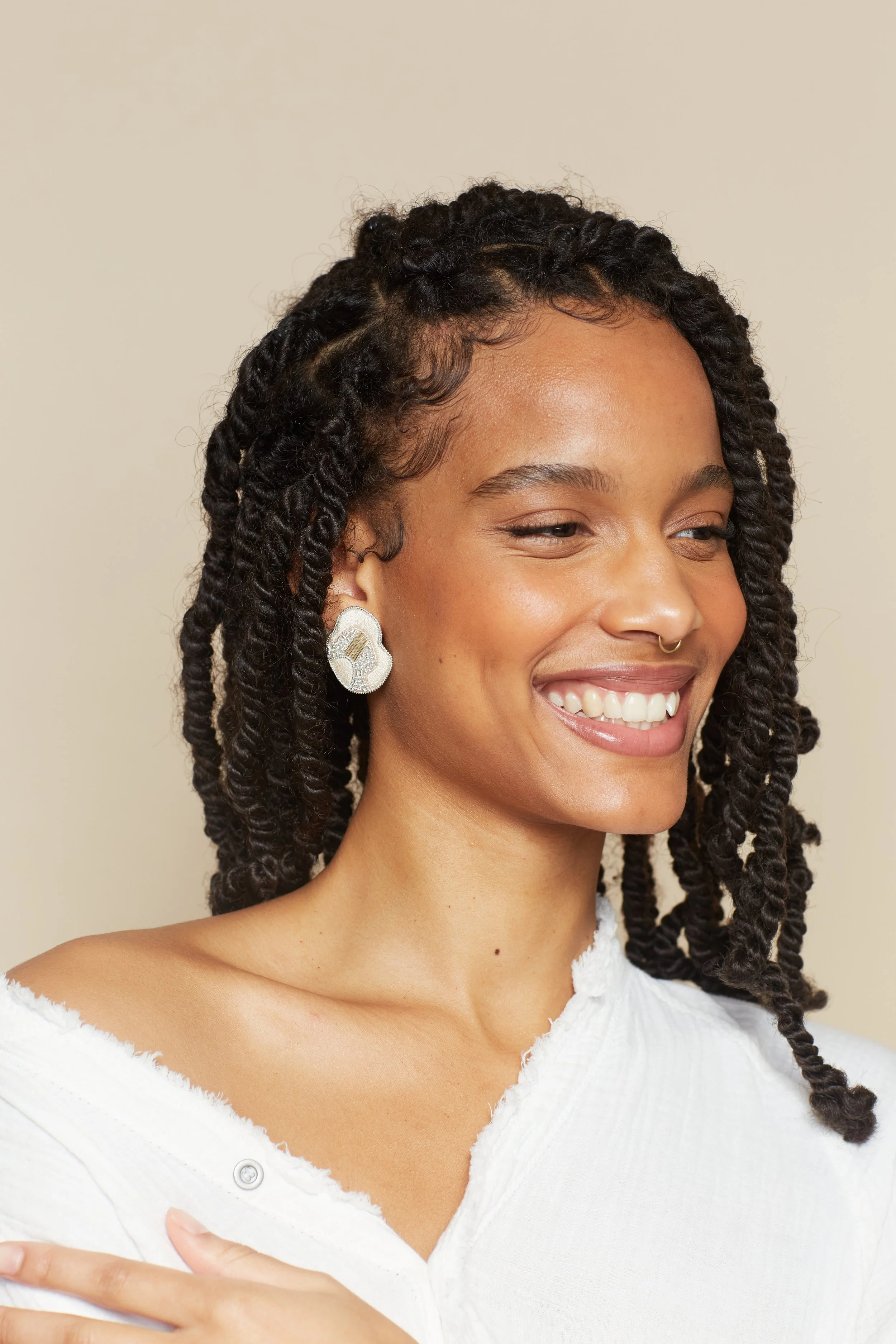 Model wearing unique organic shaped stud earrings in a neutral sand toned thread embroidery with a central accent of silver and champagne toned goldwork embroidery.