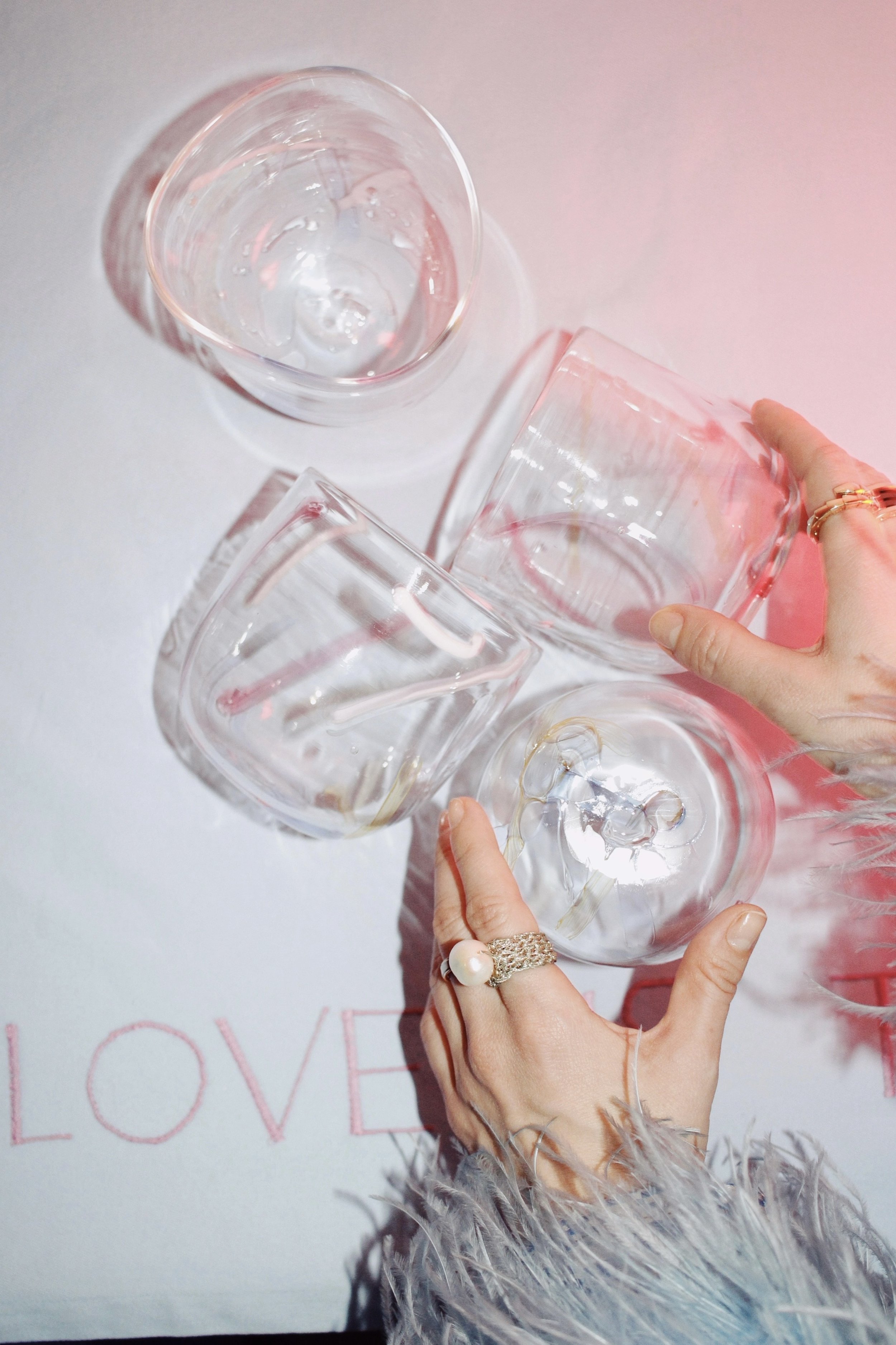 A person holding three clear glass tumblers with water, with the word 'LOVE' partially visible in pink on a white background.