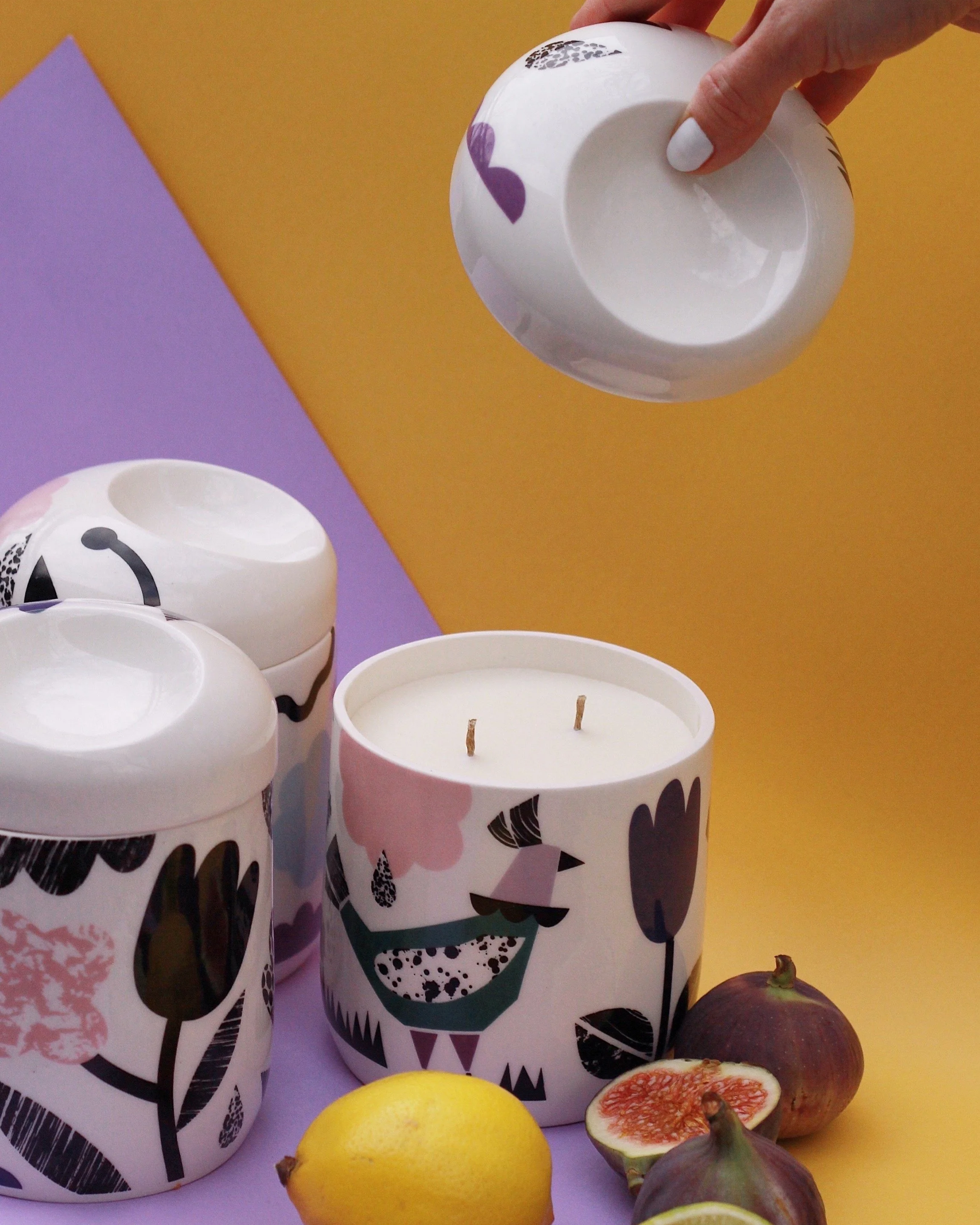 Decorative candles with fruit including lemons, figs, and a mangosteen on a purple and yellow background.