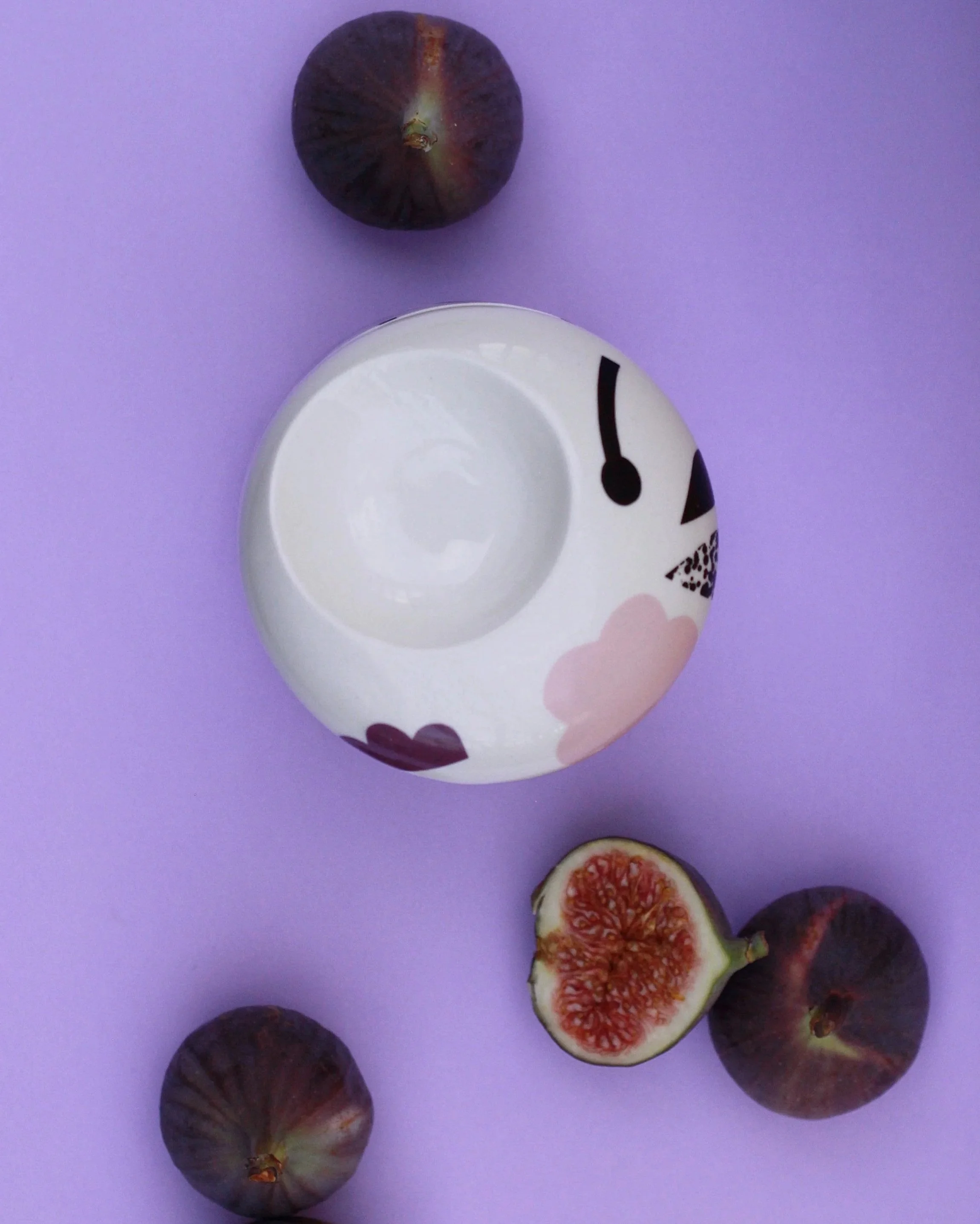 Whole and sliced figs on a purple background with a ceramic bowl.
