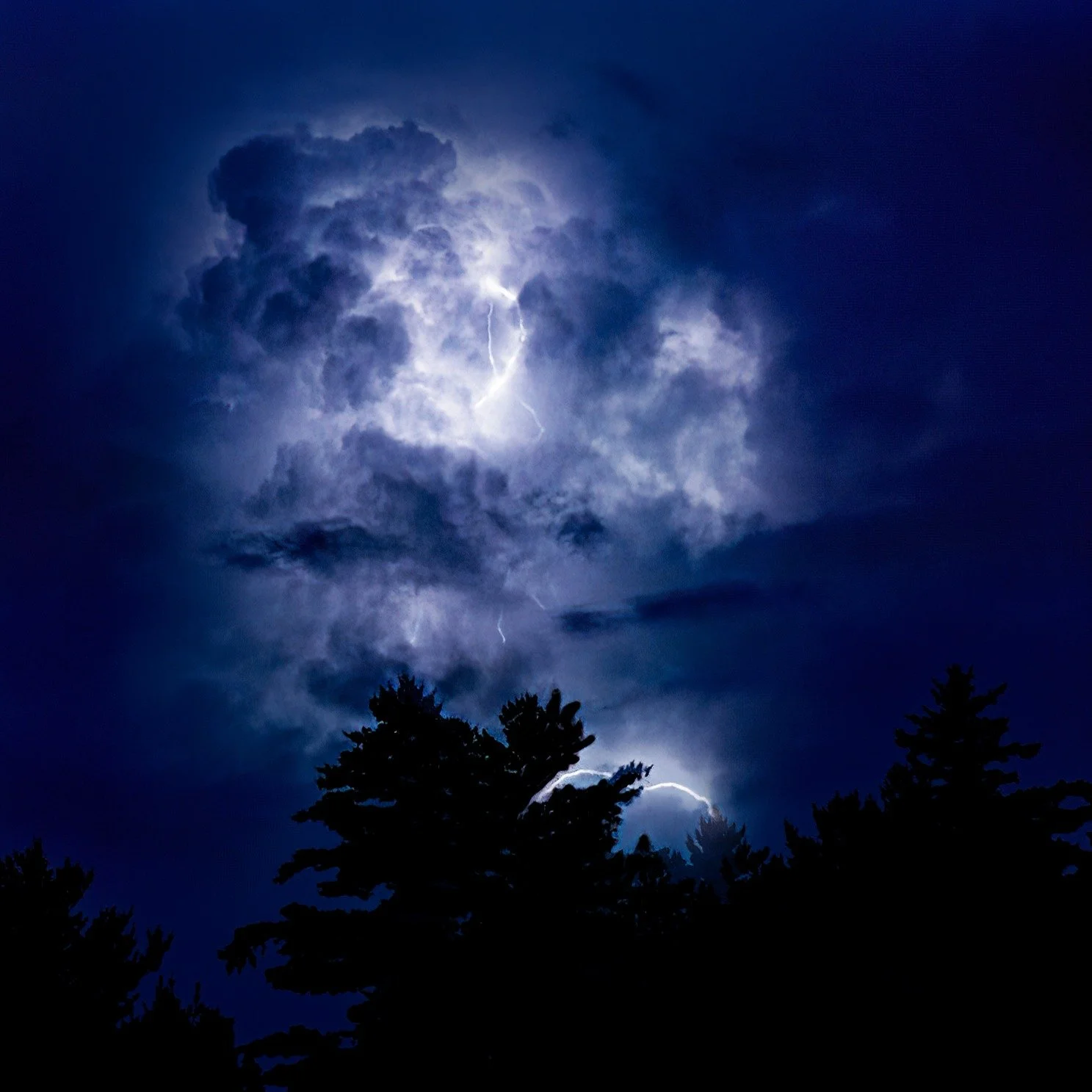 The mountains were putting on a light show.

The storm was still miles away, hidden beyond the distant ridges. Here, the air was calm and the sky above us remained quiet, but every few seconds the towering clouds erupted from within, glowing like gia