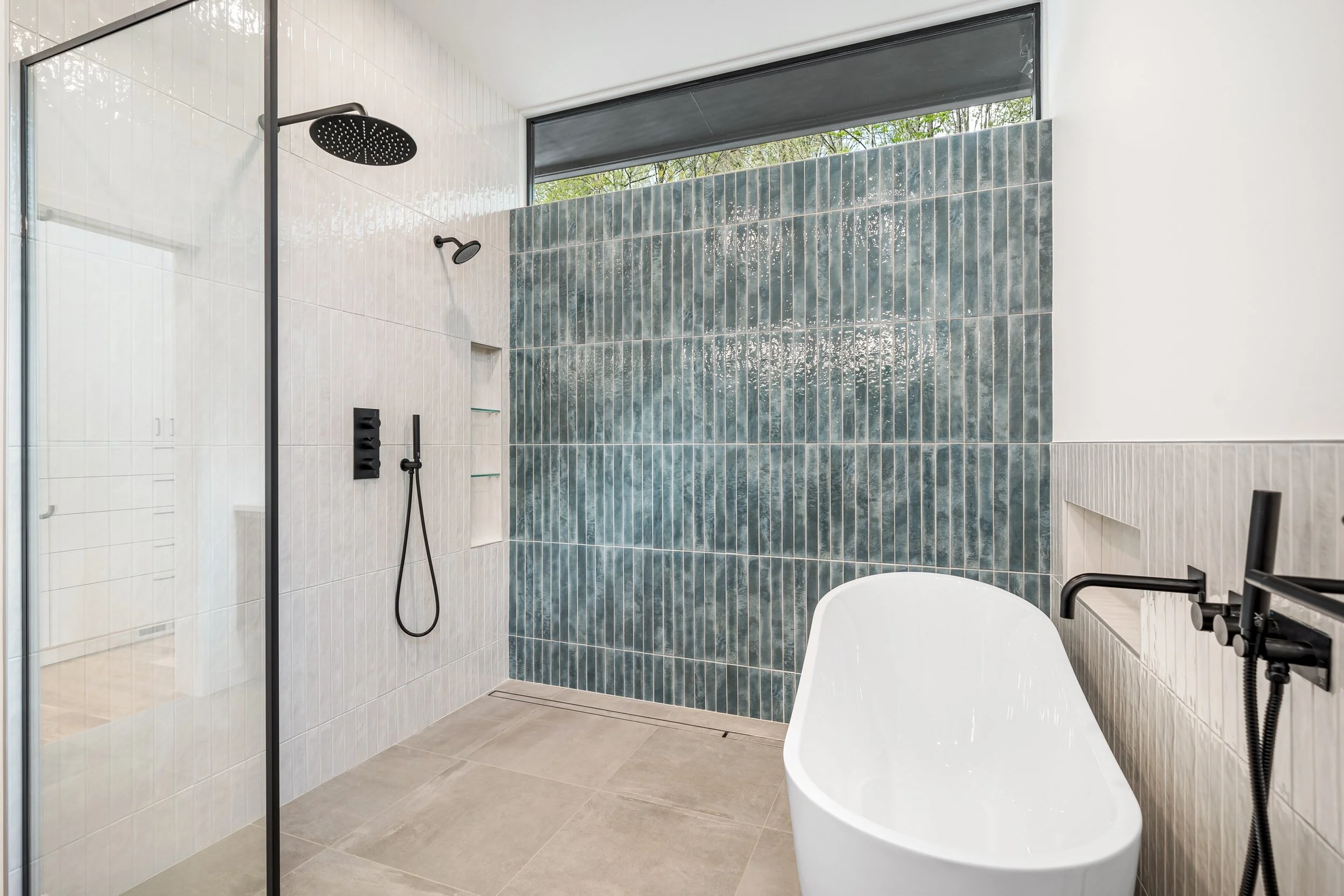  Primary bath shower area; a large high window above a colorful tile accent wall complements the clean minimal space. 